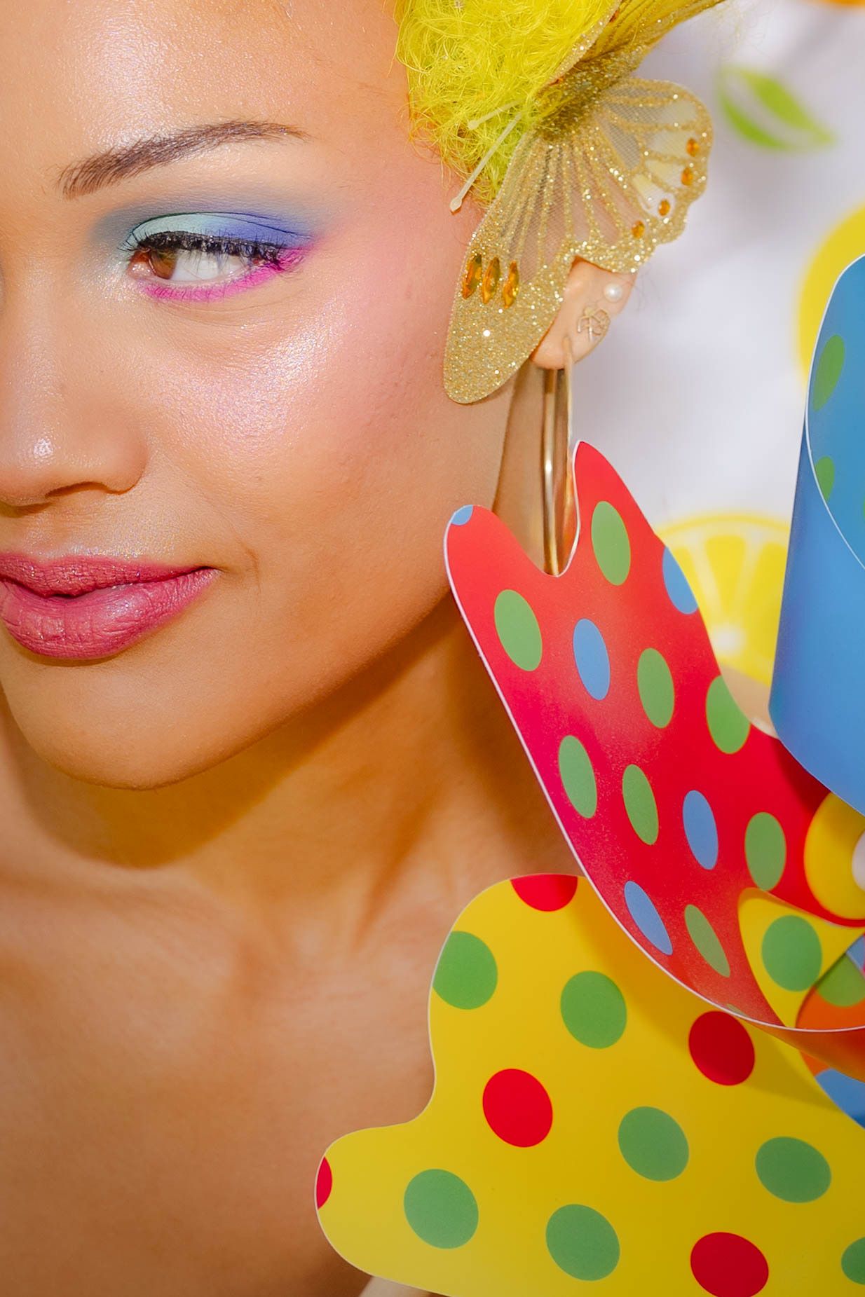 Close-up beauty shot with vibrant yellow hair accessory and colorful polka dot pattern in background.