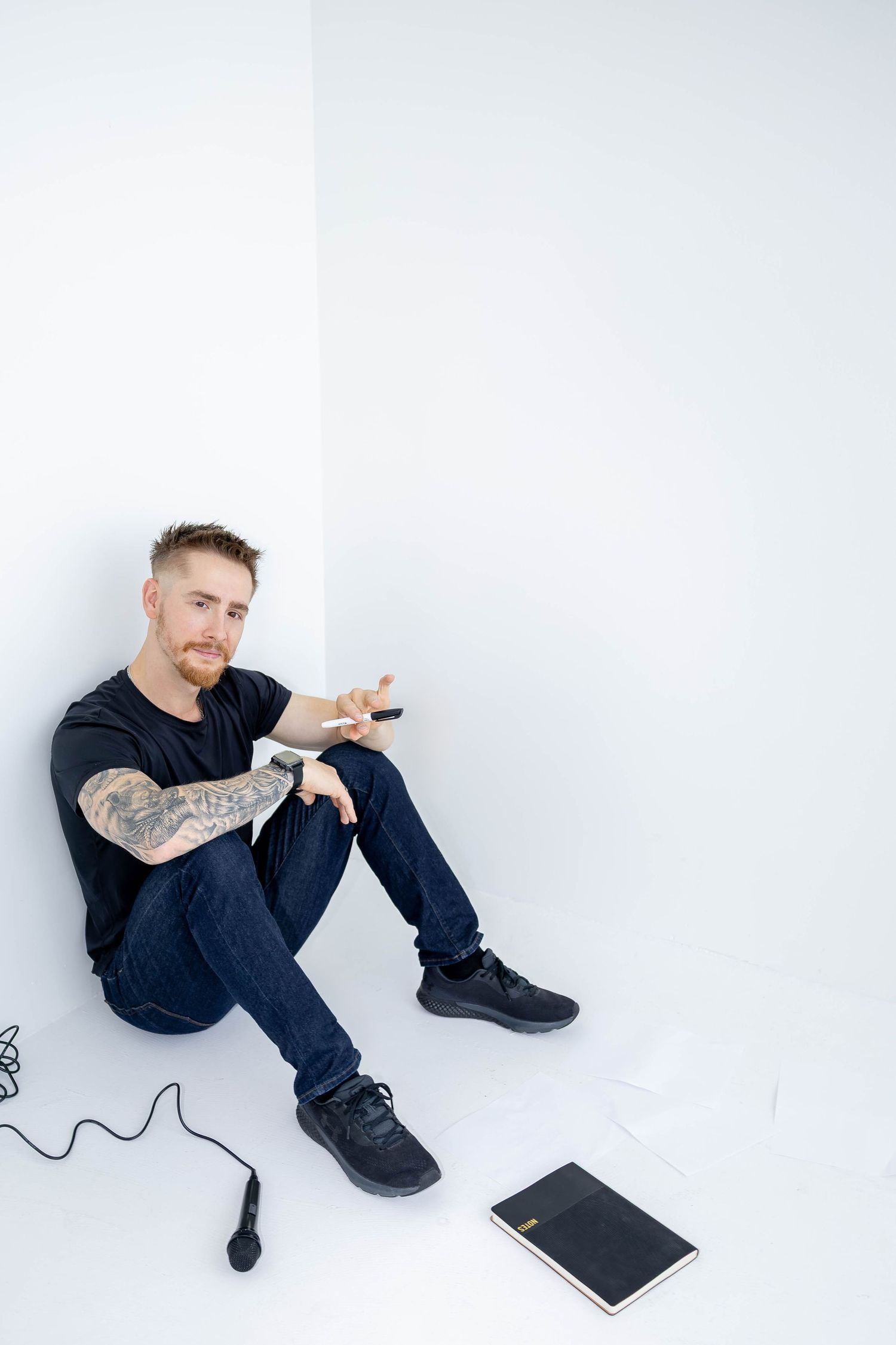 Person in black clothing sitting on white floor interacting with digital tablet in minimalist setting.