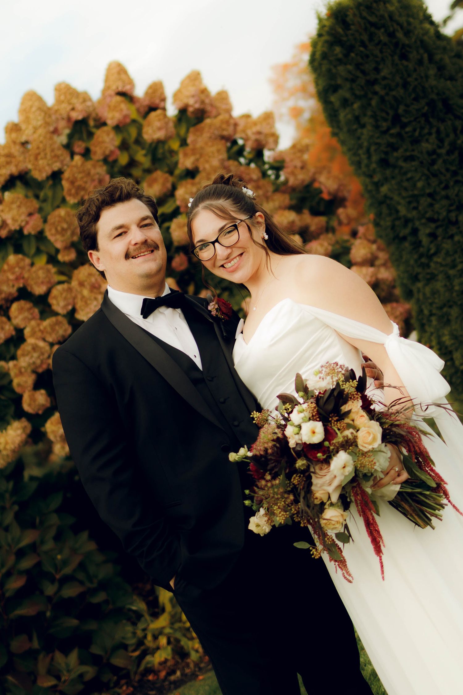 A romantic wedding couple poses against an autumn backdrop with dried hydrangea flowers.