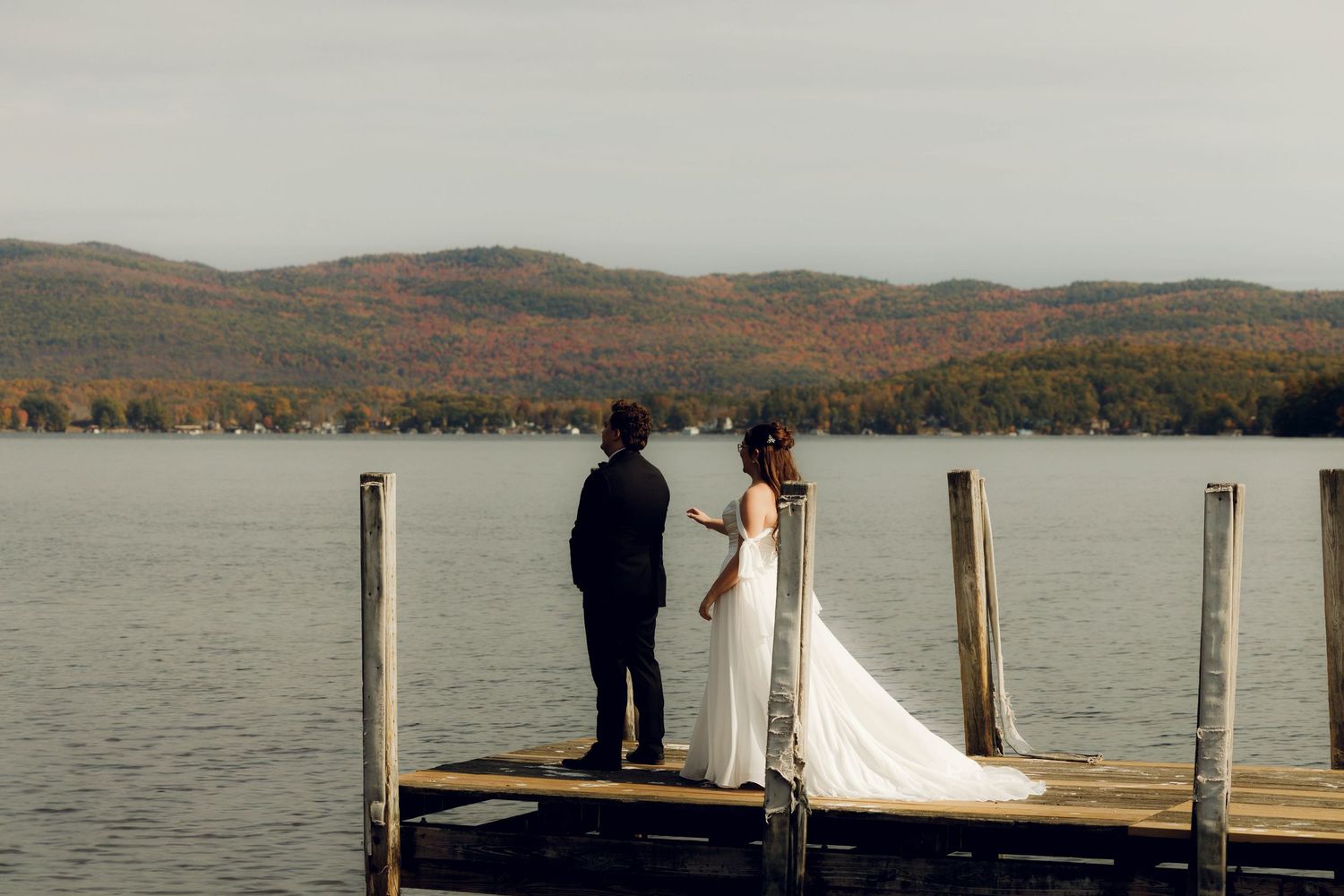 Wedding ceremony and reception on a lakeside dock with autumn foliage in the background during sunset.
