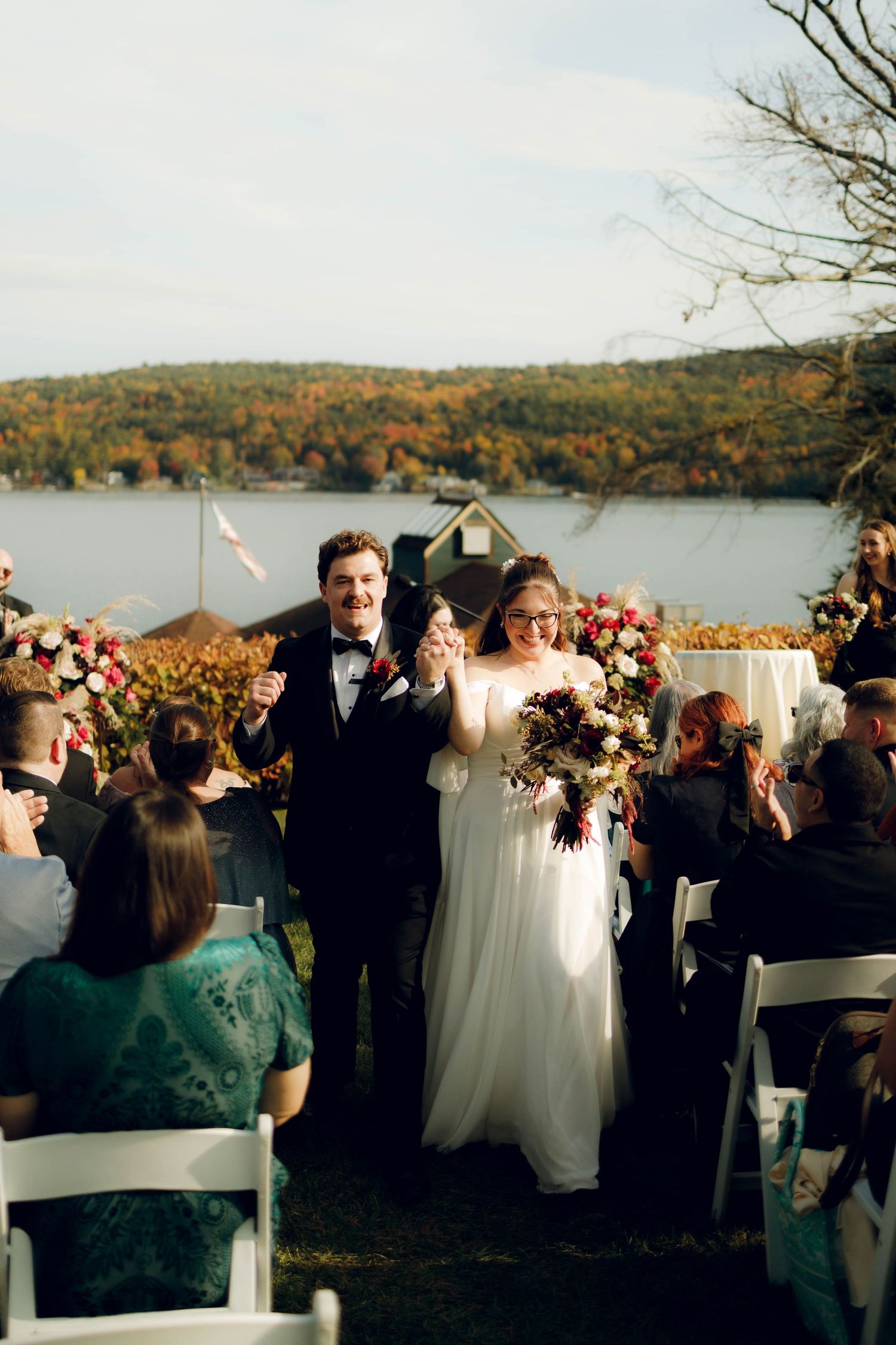 Outdoor wedding ceremony overlooking a scenic autumn lake with fall foliage on surrounding hills.