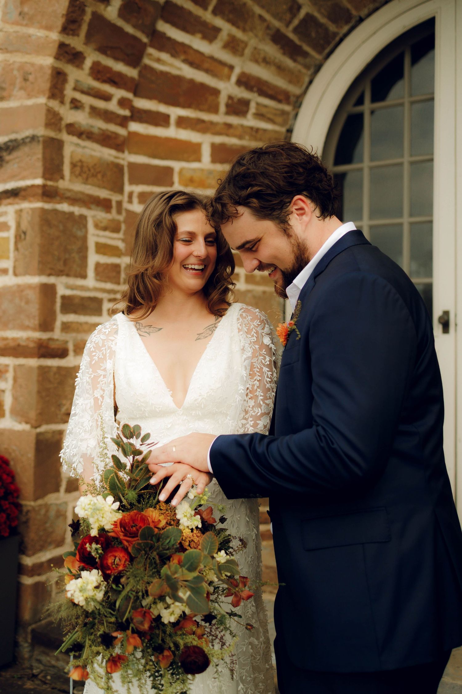 A romantic wedding moment captured in a brick archway with a couple holding a red and green bouquet.