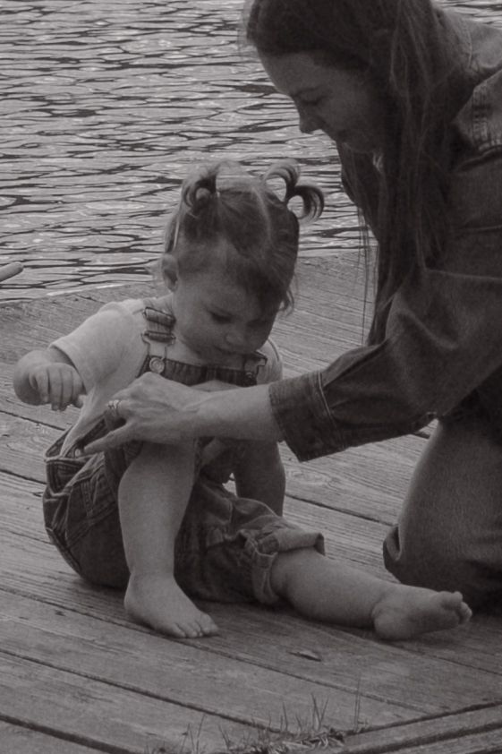 A series of black and white photographs show someone drawing with chalk on wooden deck boards near water.