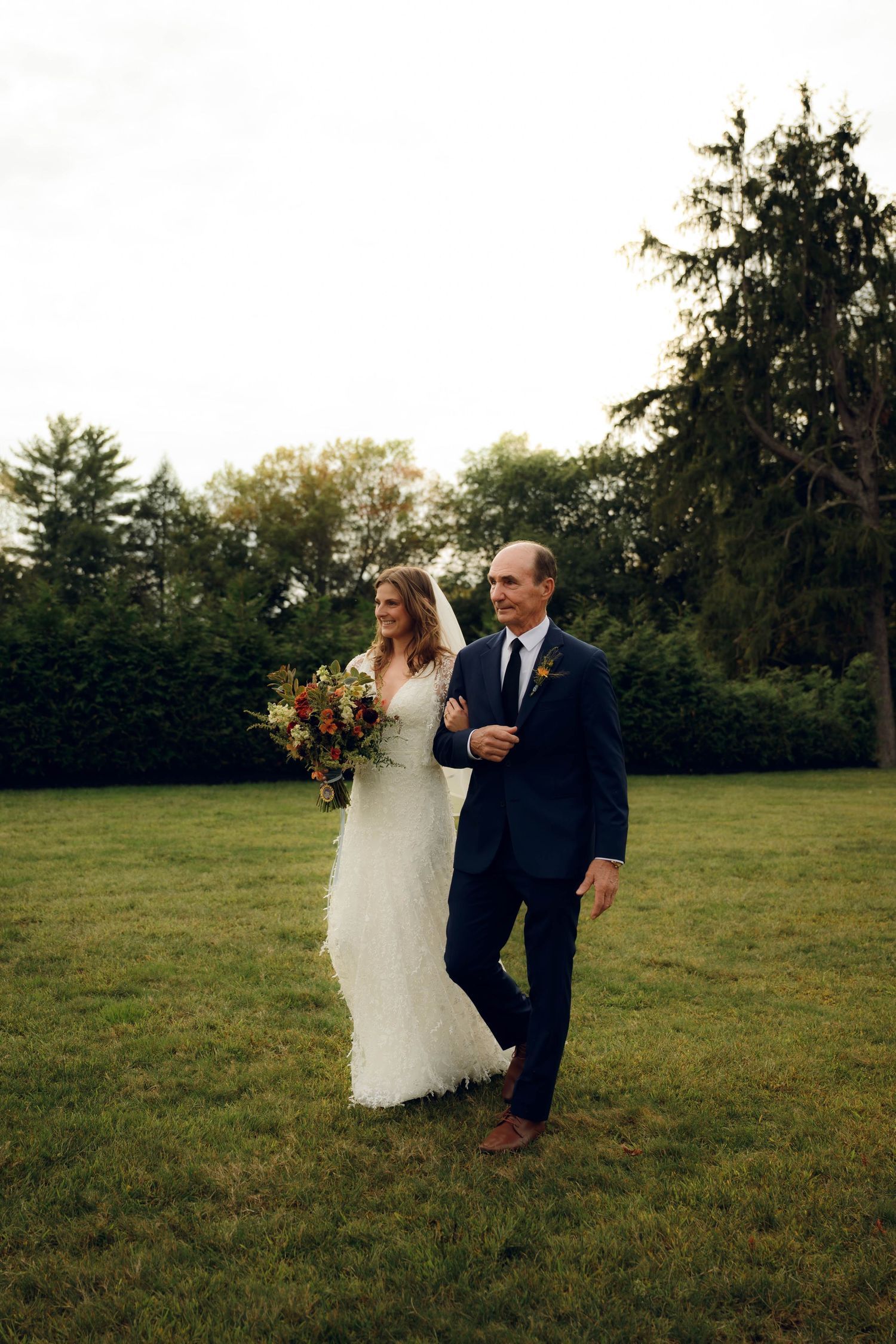 A couple shares a romantic moment dancing together on a grassy field during their outdoor wedding celebration.