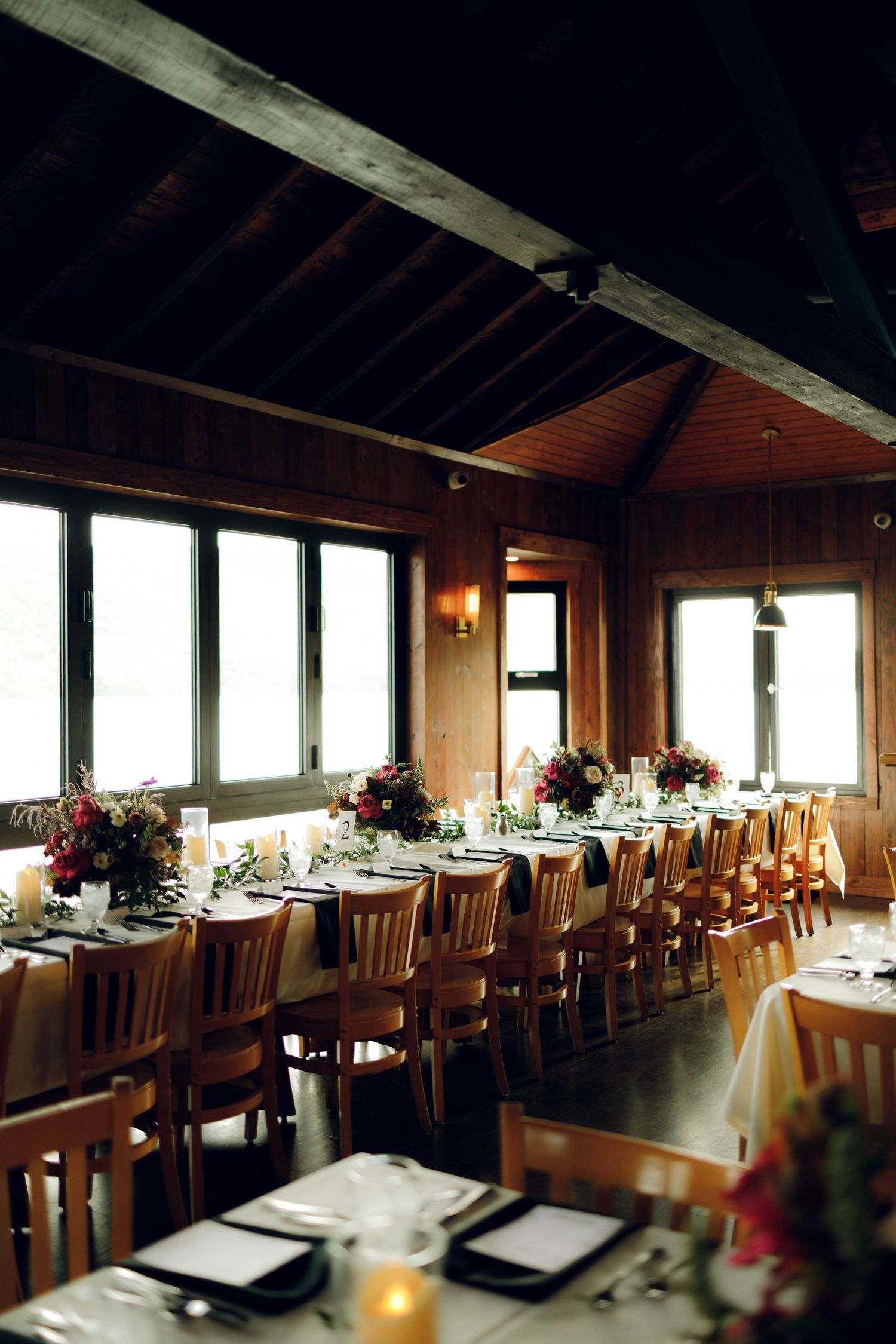 Long wooden dining tables with elegant place settings line a rustic restaurant interior with panoramic windows.
