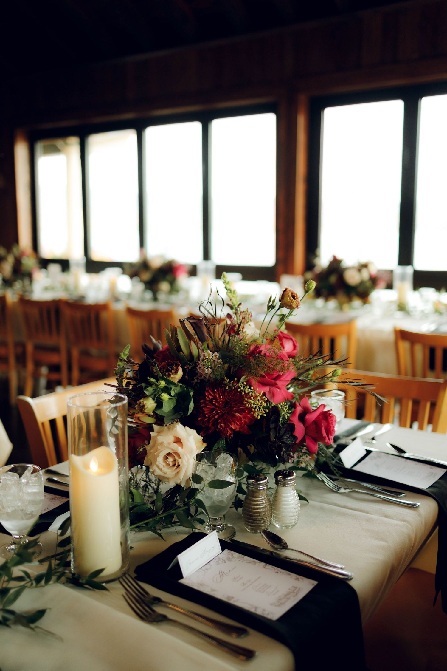 Elegant wedding reception tables decorated with white candles and floral arrangements in a rustic indoor venue.