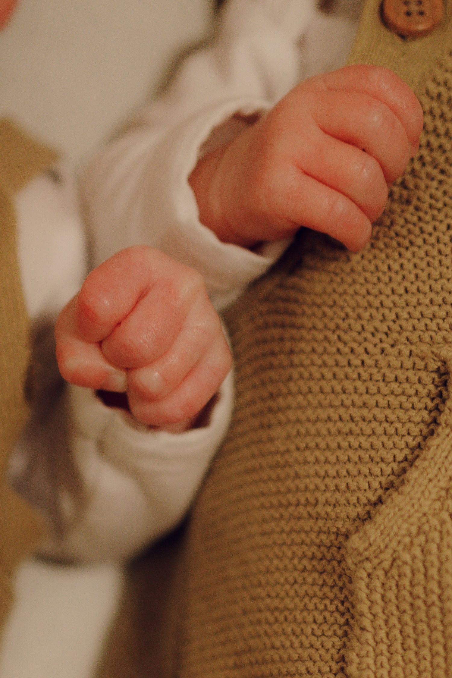 Close-up series showing tiny baby hands reaching and grasping against a tan knitted fabric background.