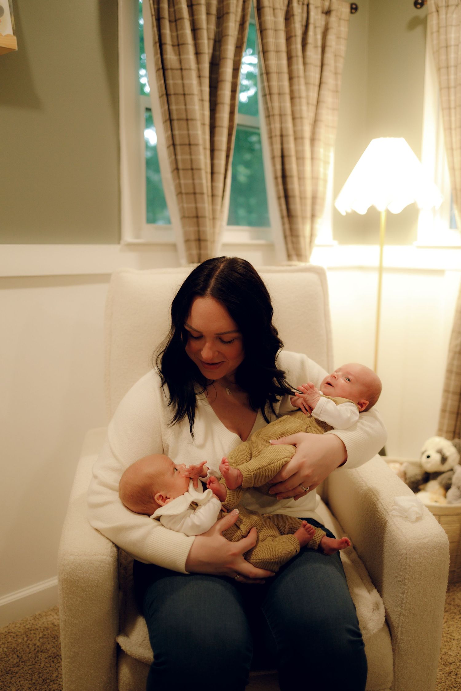 A mother lovingly feeds and bonds with her infant in a cozy nursery with soft lighting and plaid curtains.