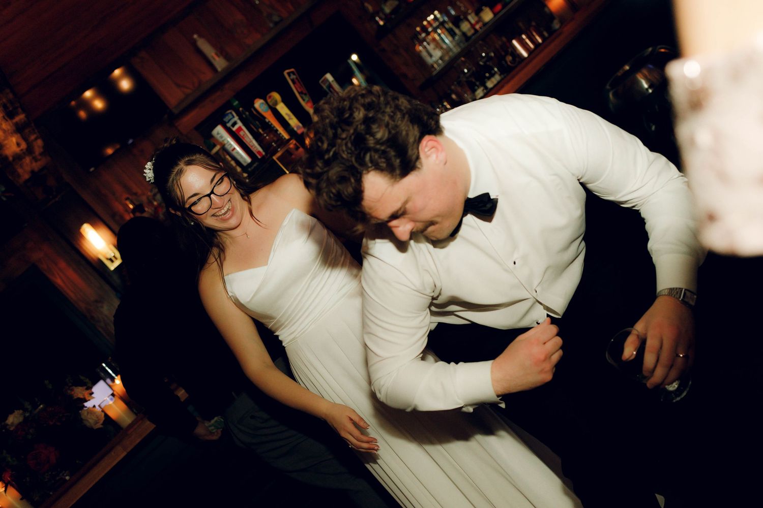 A couple in white attire share a joyful dance moment together at an evening celebration.