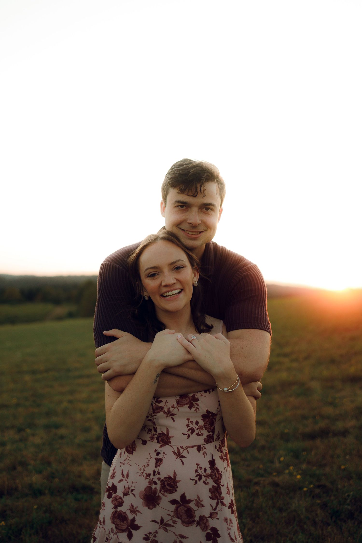 Couple embracing in a field during golden hour sunset.