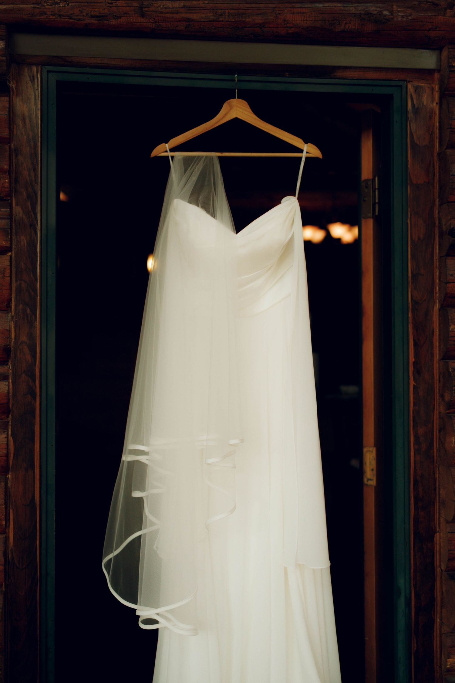 A white wedding dress veil hangs elegantly on wooden hangers against a dark background.