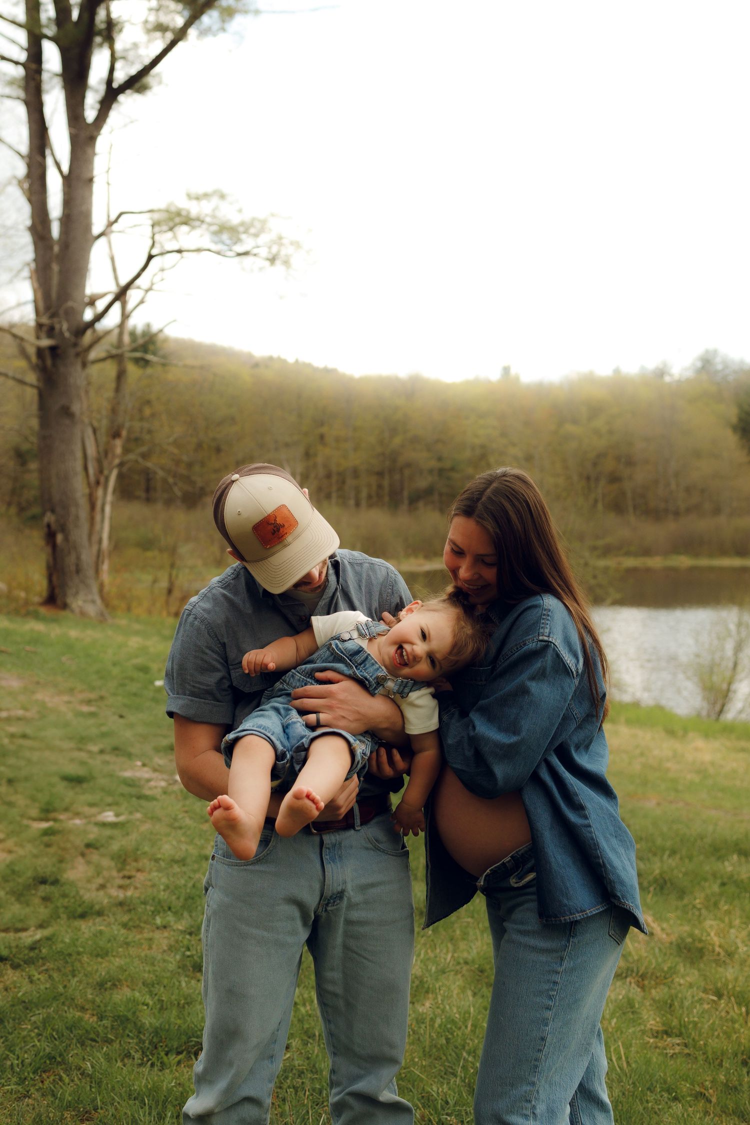 A family shares a playful moment together on a grassy hill near a lake during a sunny afternoon.