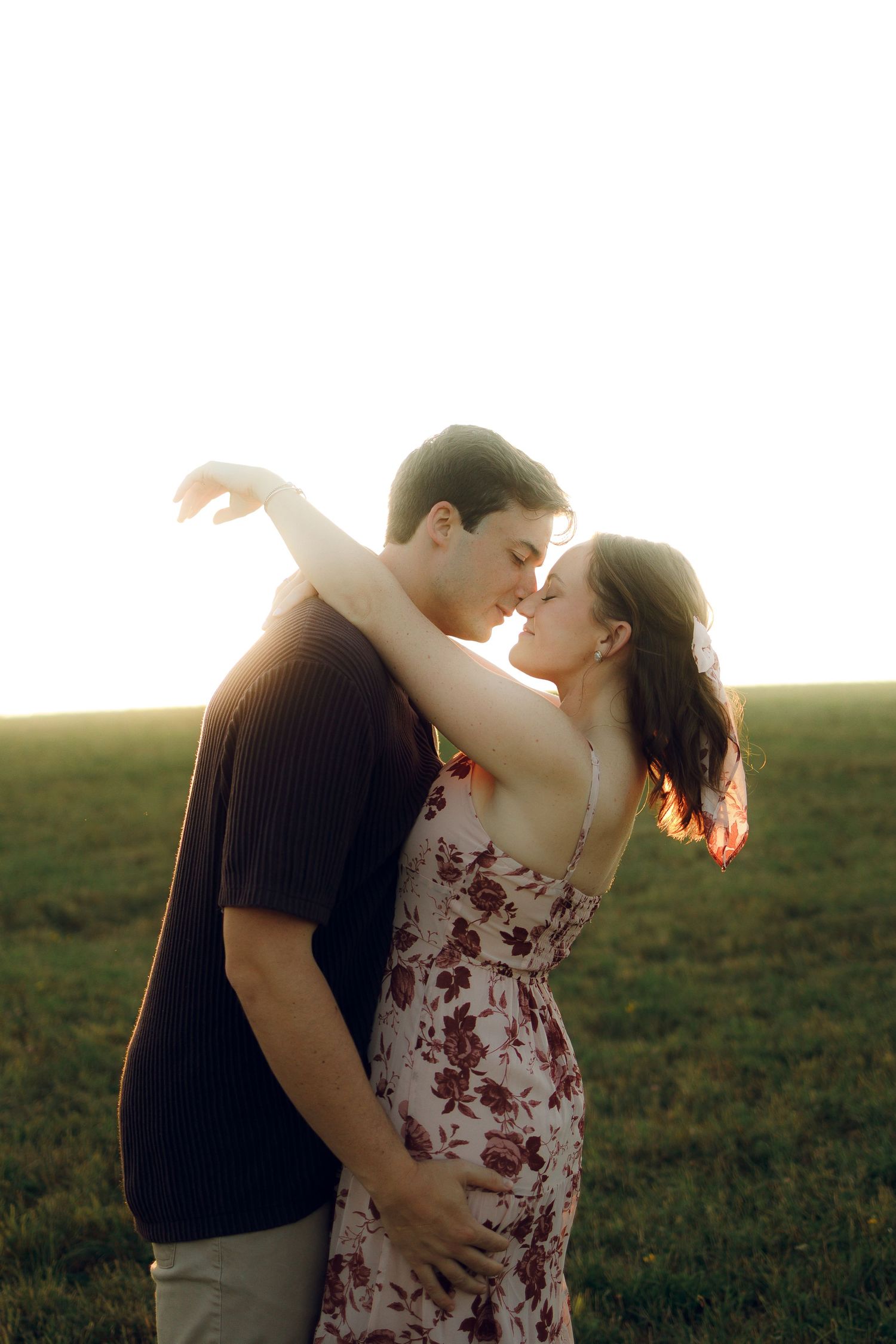 Romantic couple embraces in a grassy field at sunset, creating a series of intimate silhouettes against the golden sky.