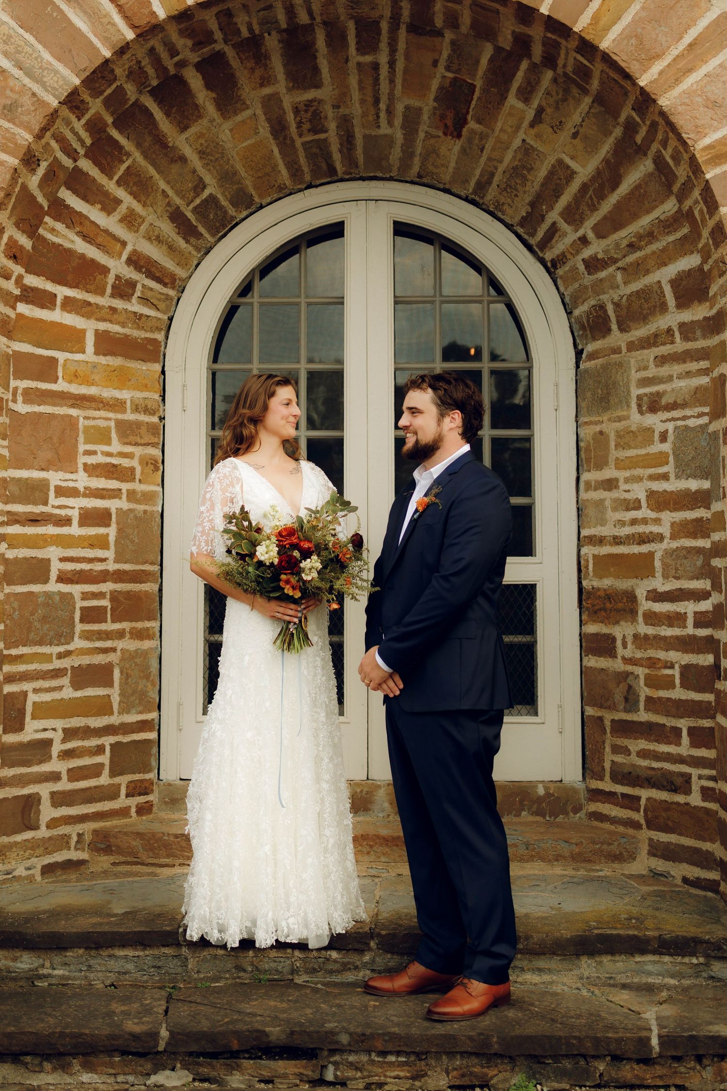 A couple shares a romantic moment under a rustic brick archway during their wedding photo session.