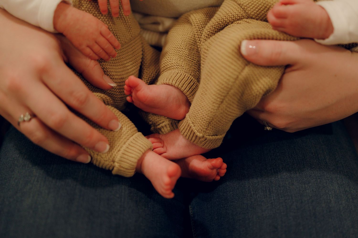 Close-up of tiny baby feet in tan knit socks being held by gentle hands.