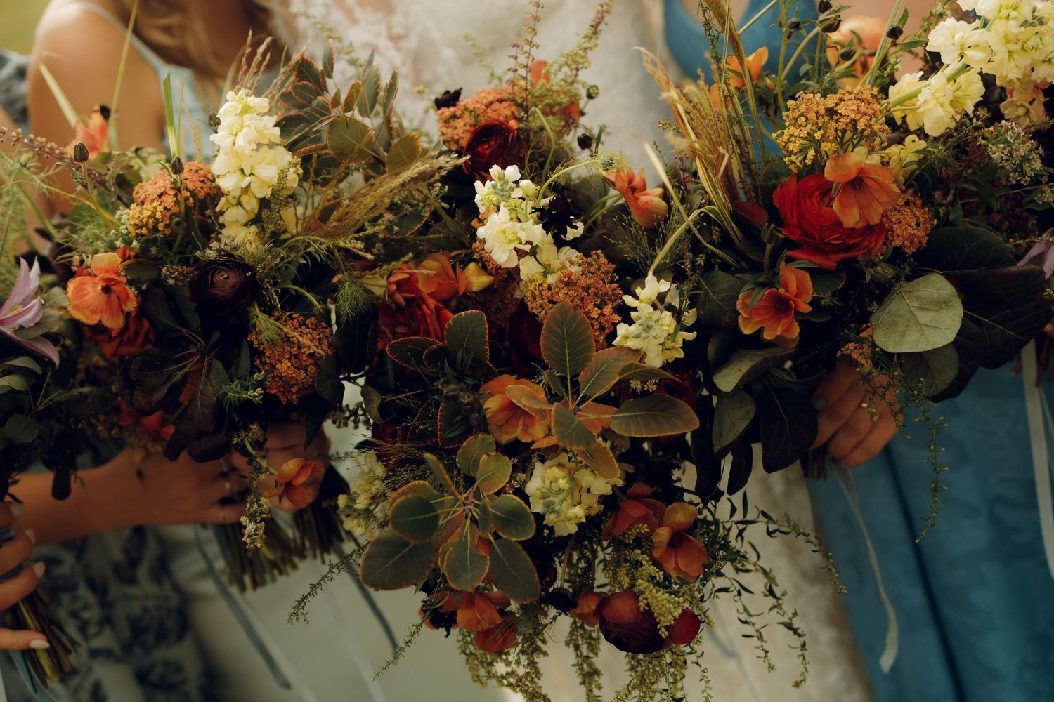 A lush autumnal floral arrangement with red, orange and cream flowers mixed with wild grasses and greenery.
