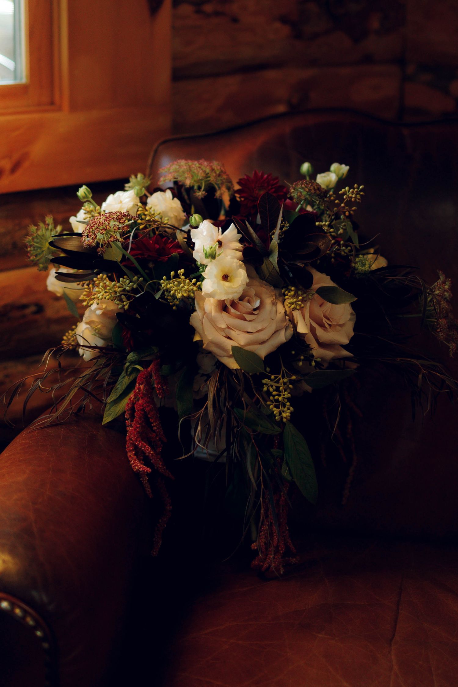Elegant floral arrangements in dark glass vases with white roses and greenery displayed on wooden surface in dim lighting.