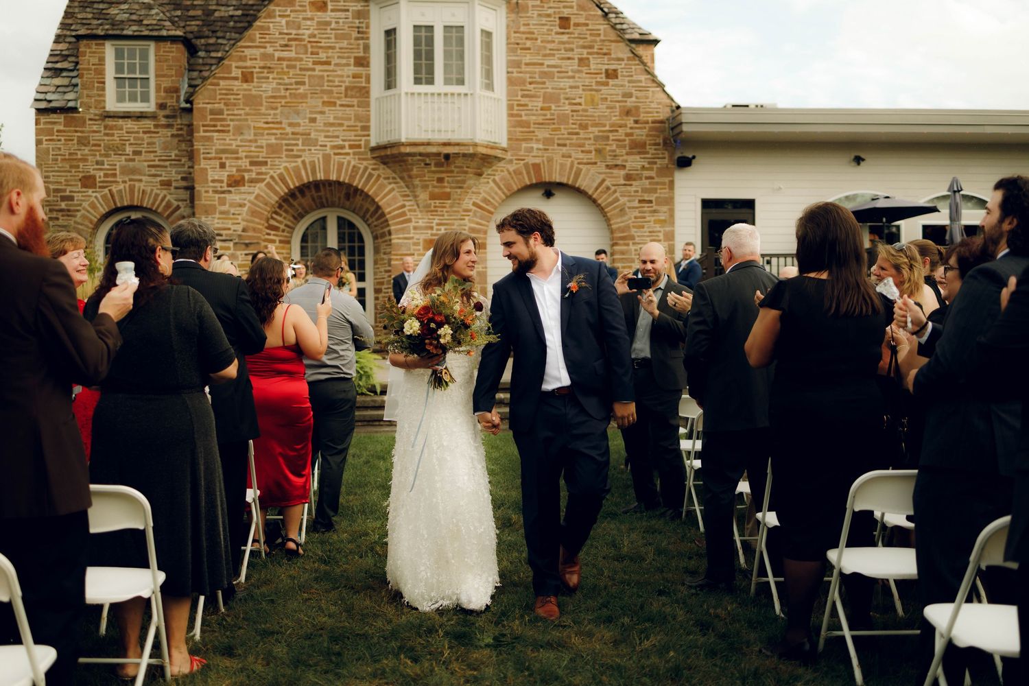 Wedding guests gather outside a historic brick building during a daytime outdoor reception celebration.