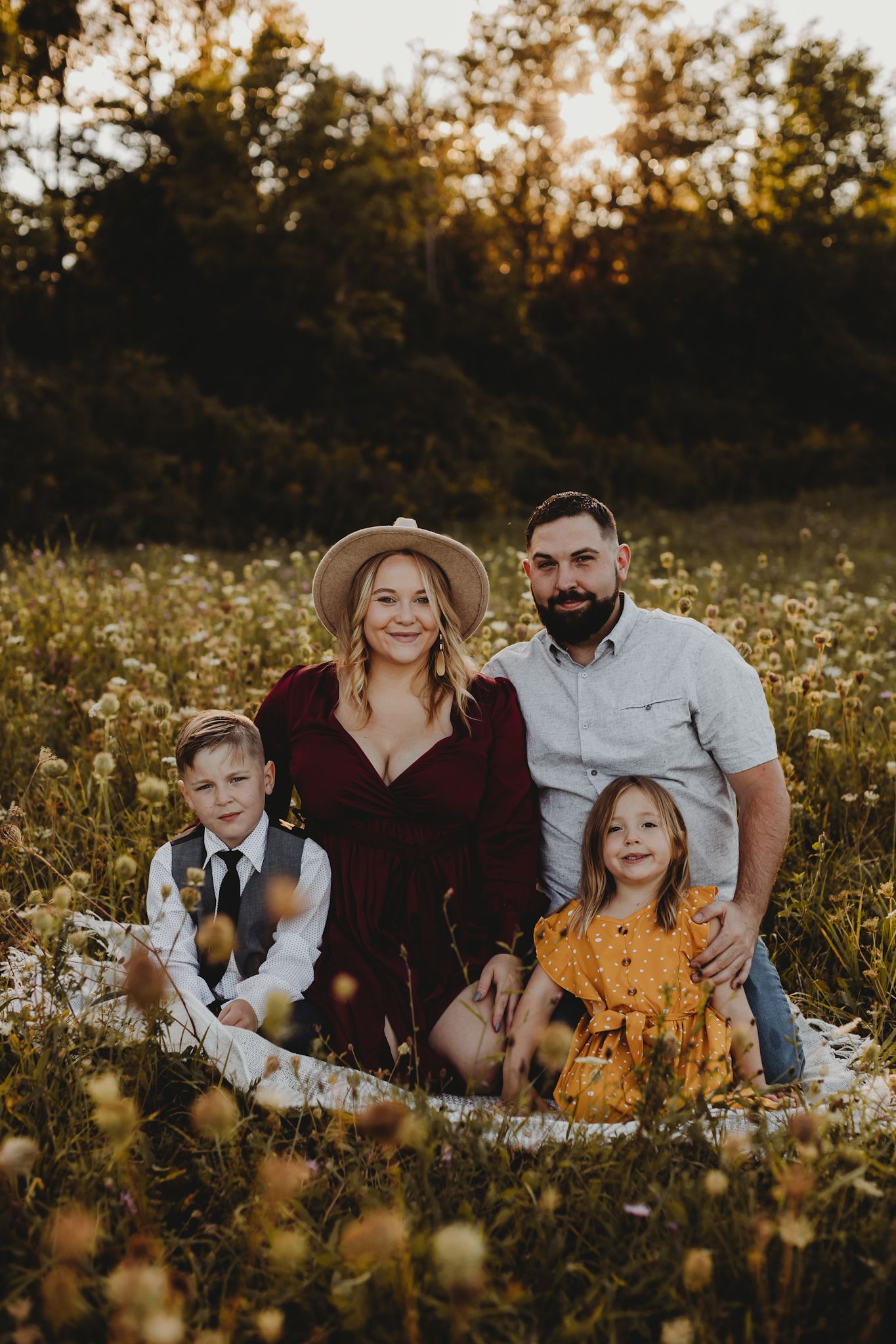Family sitting together in a wildflower meadow at golden hour with warm sunset lighting in the background.