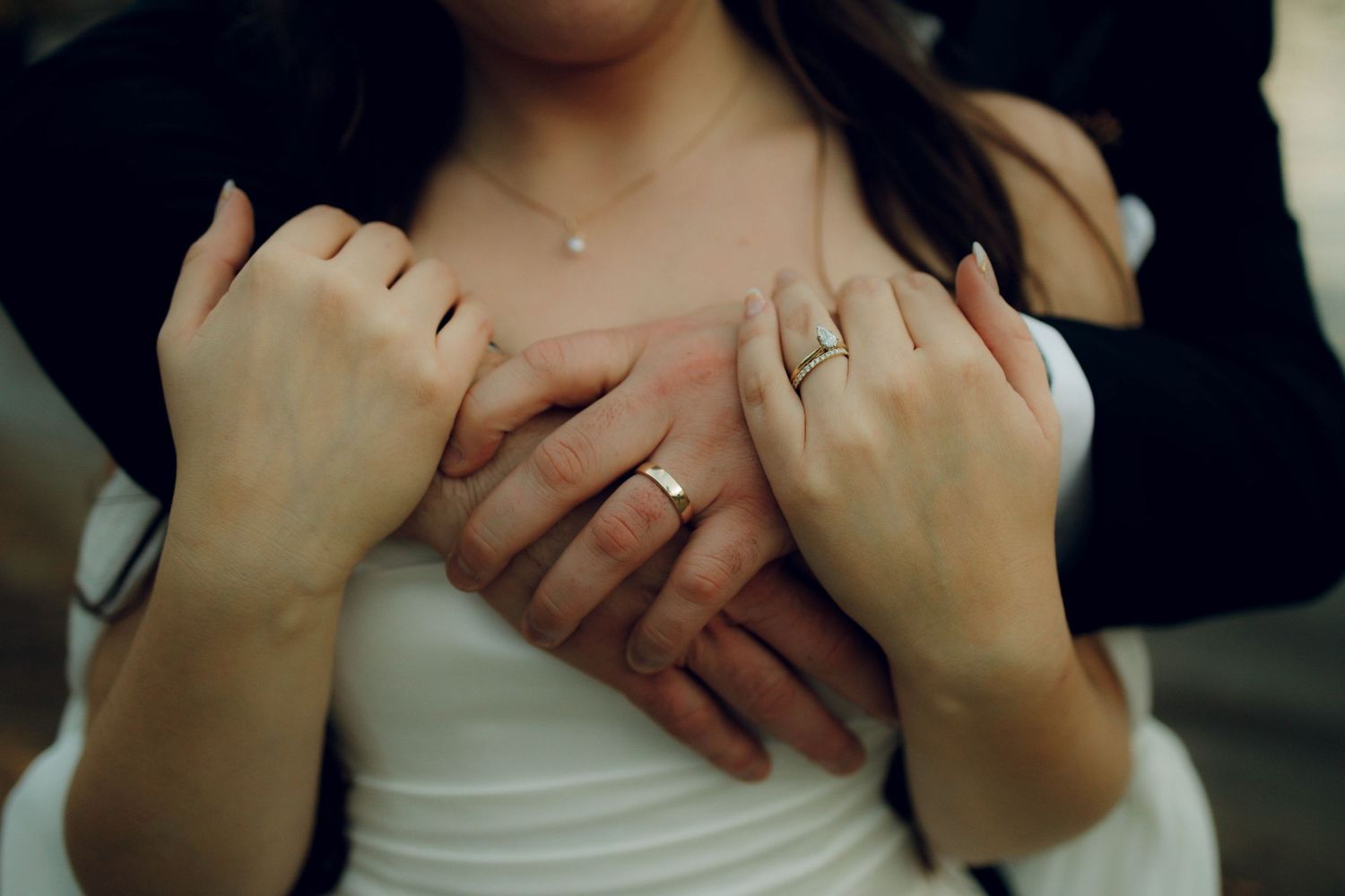 Close-up photo of hands holding each other in tender gestures against a dark background.