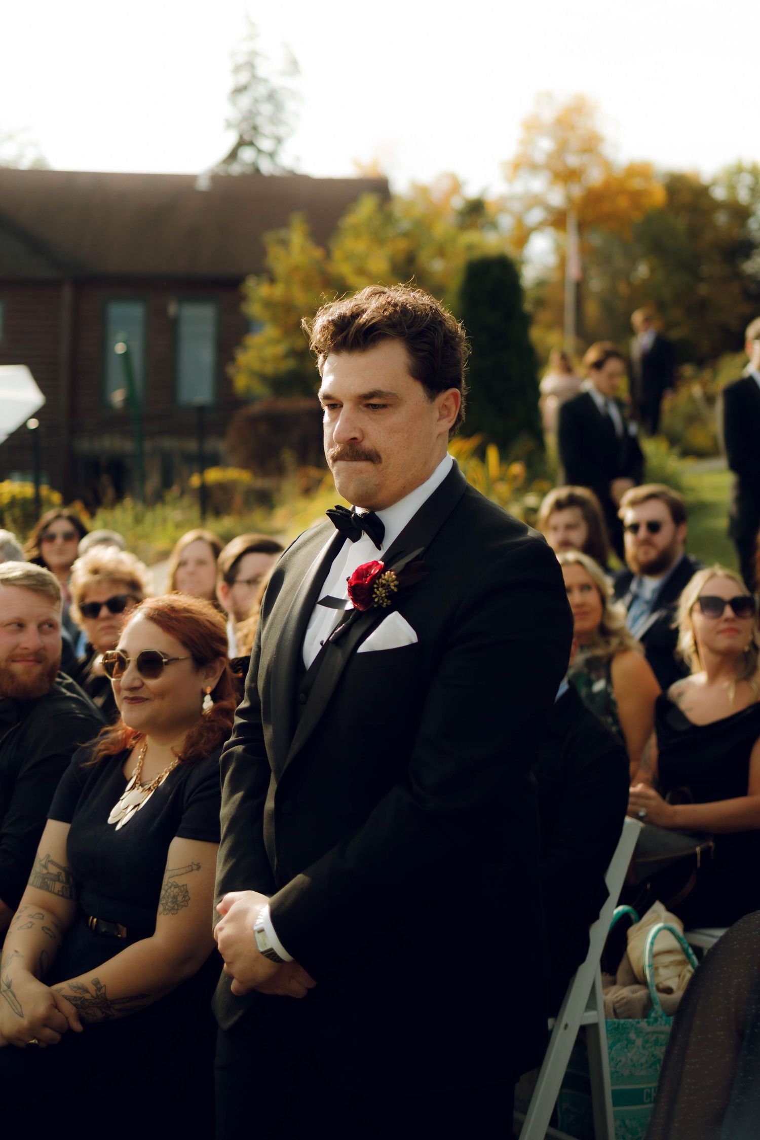 Wedding guests wearing black formal attire gather outdoors during a ceremony at sunset.