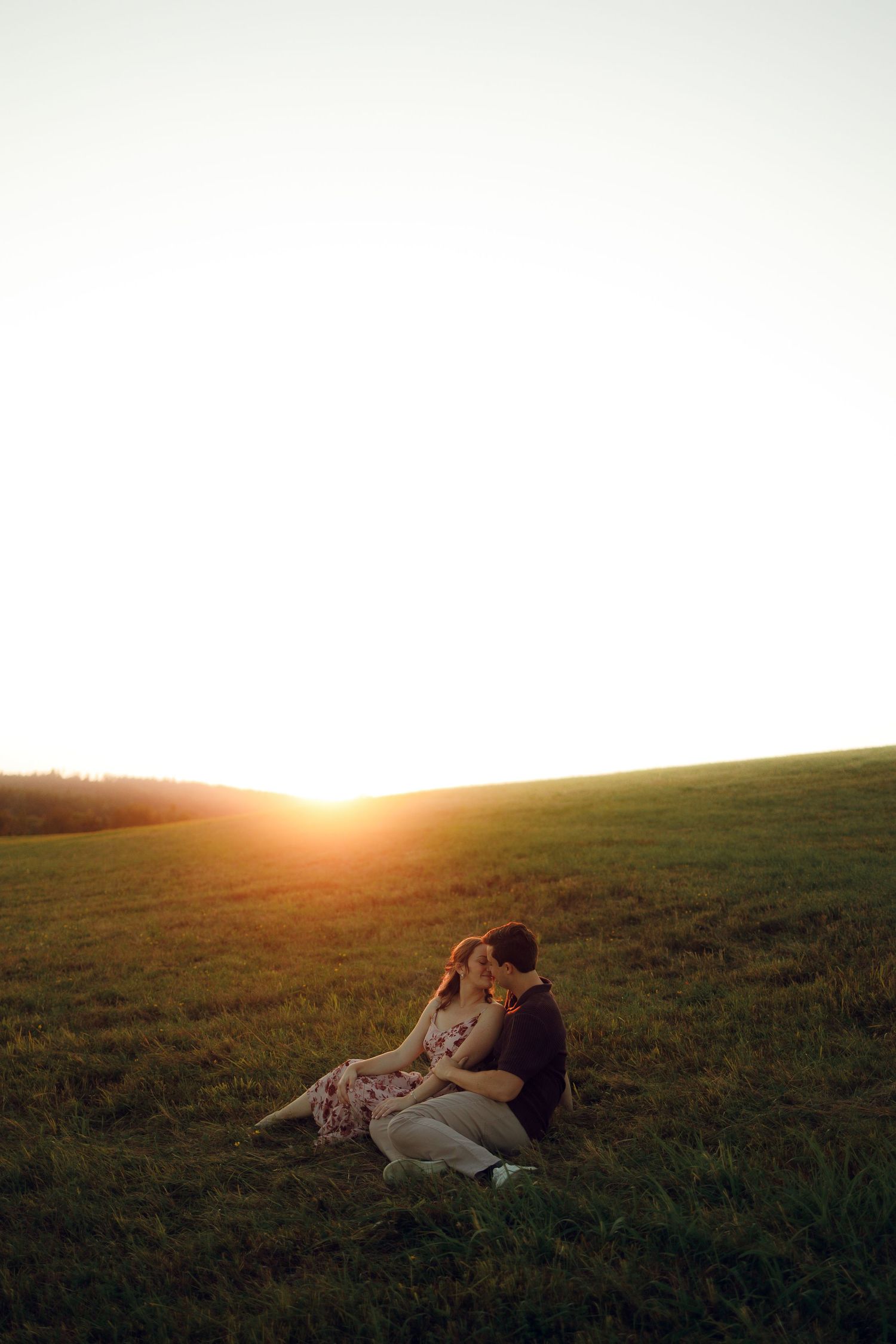 A couple and their dog lay in a grassy field at sunset, creating a warm and intimate silhouette against the golden sky.