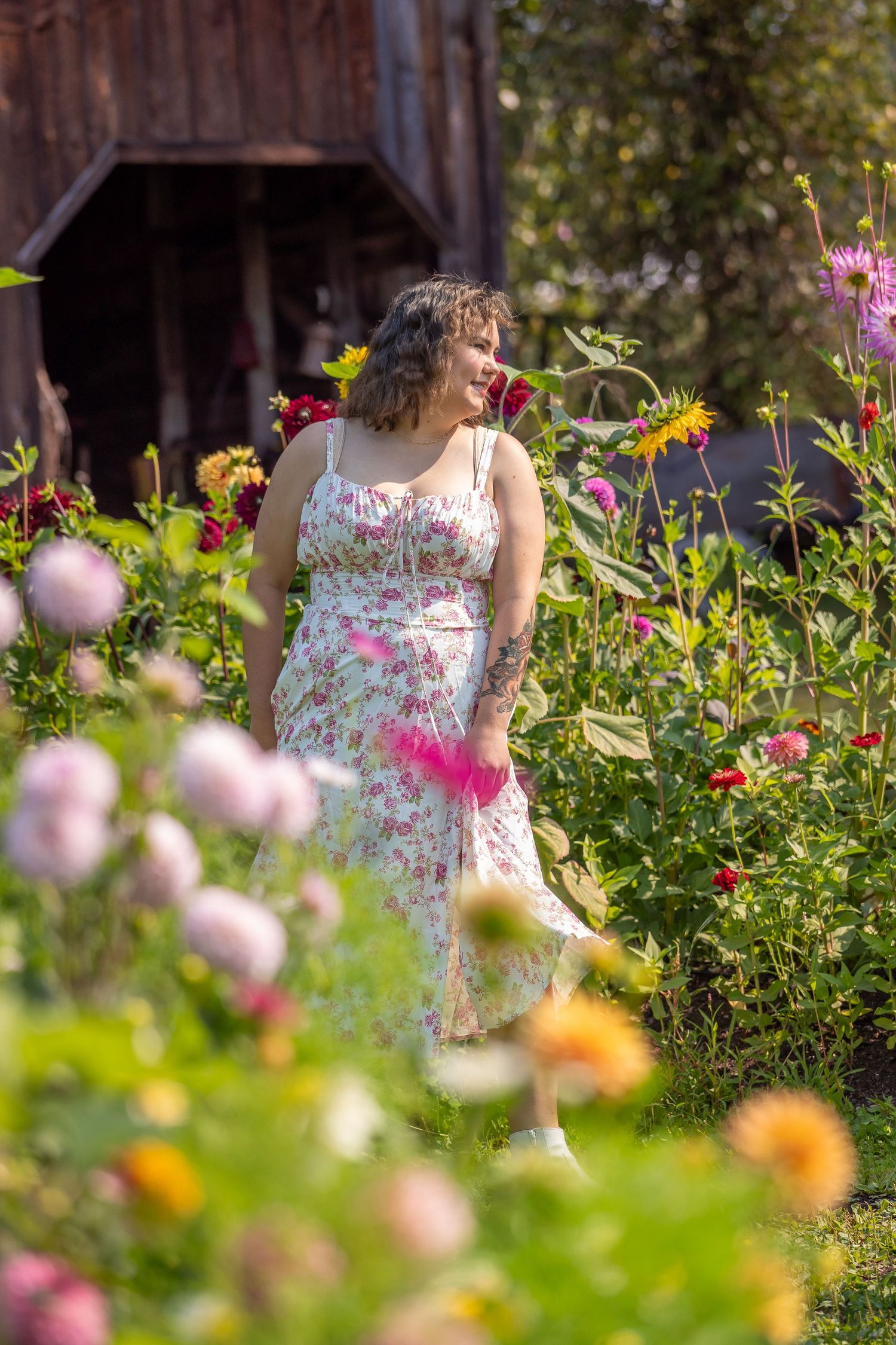 A person in a floral dress stands amid a vibrant garden of colorful summer flowers.