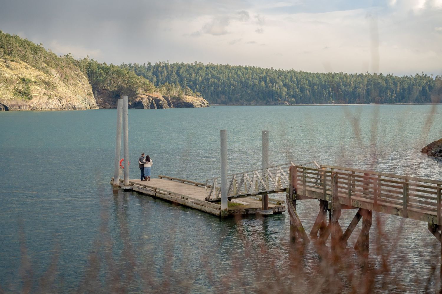 Wooden dock extending into turquoise lake surrounded by forested cliffs.