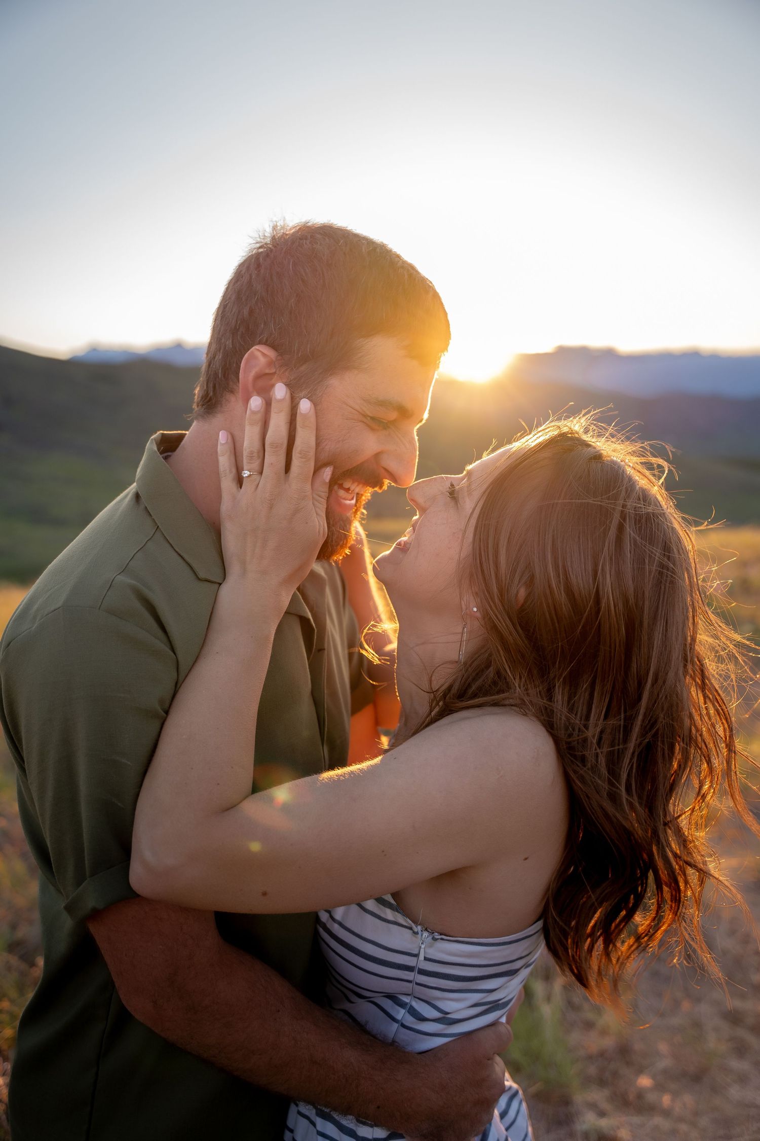 Couple sharing intimate moment at sunset with mountains in background.