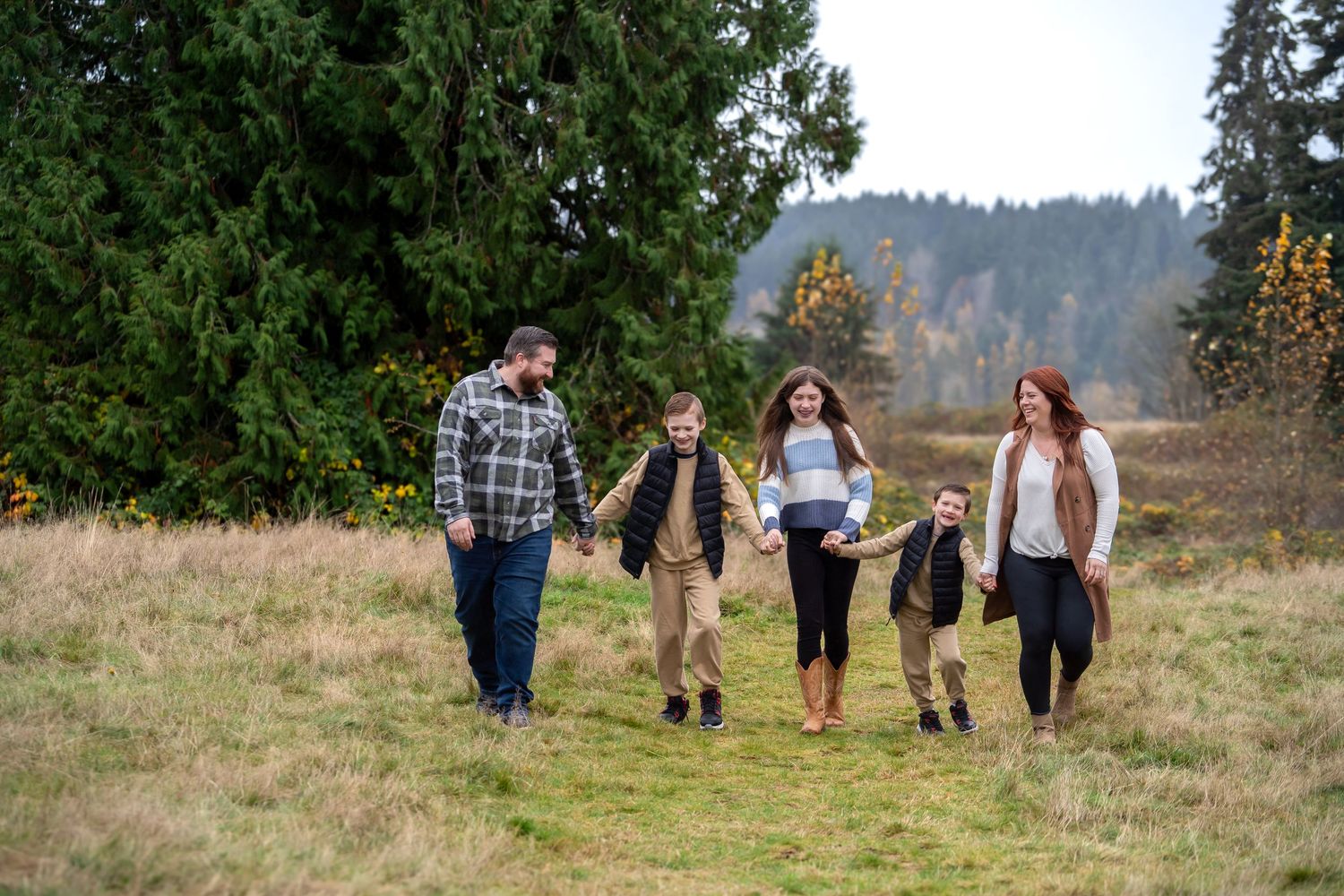 Group walking together on autumn trail through meadow with evergreen trees.