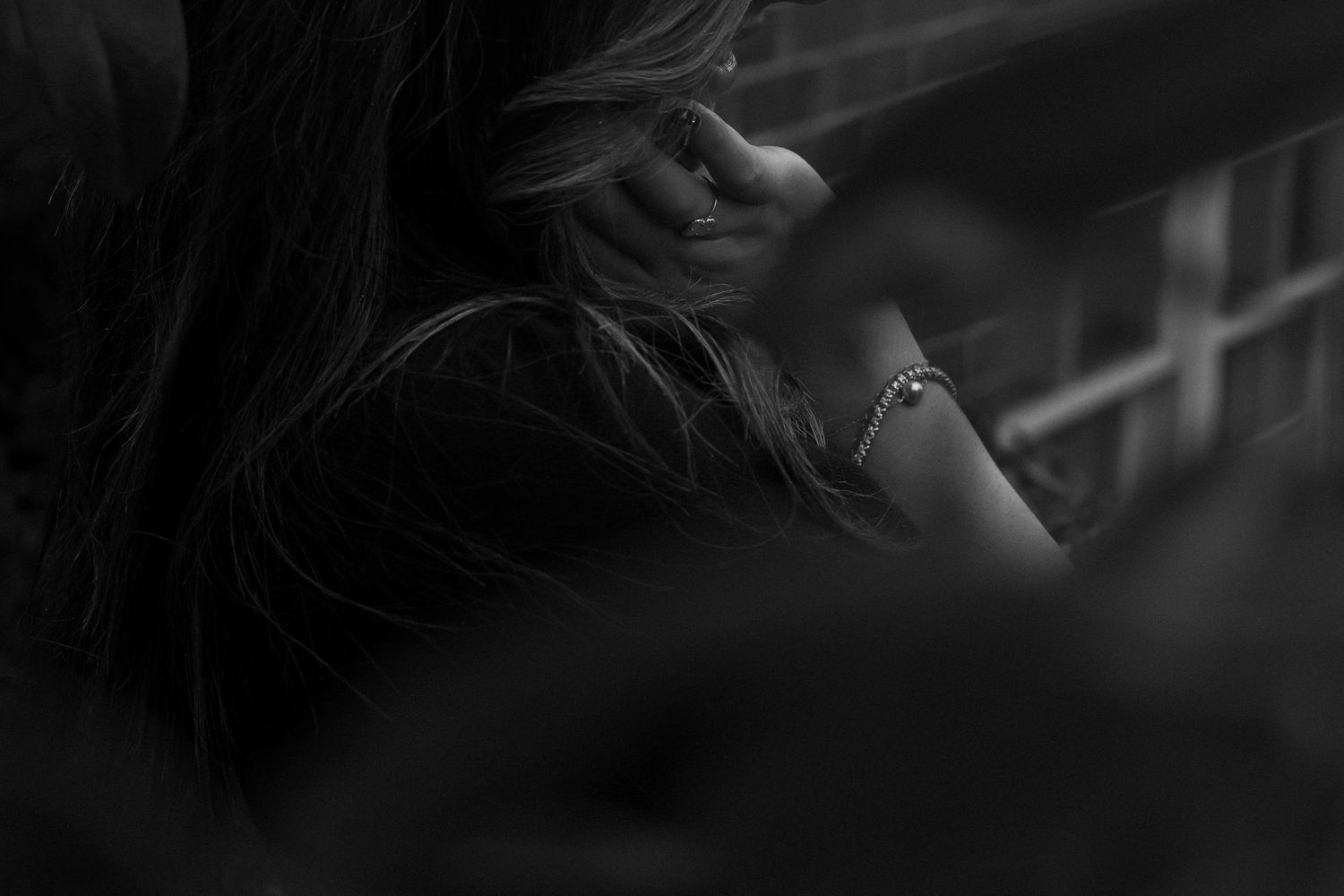A moody black and white close-up photograph highlighting jewelry and flowing hair.