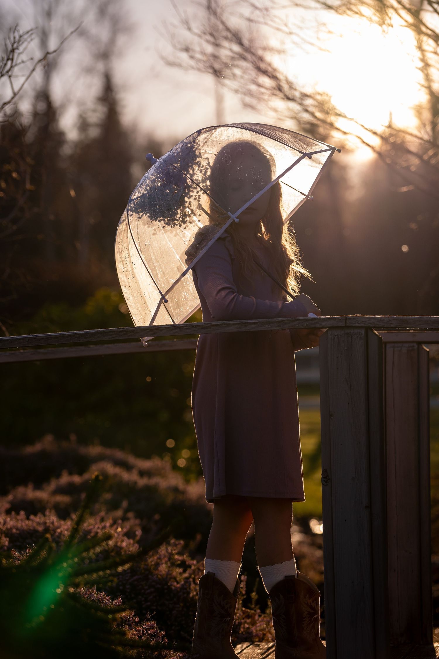 A silhouetted figure with an umbrella stands against a backlit sunset creating a dreamy atmospheric scene.