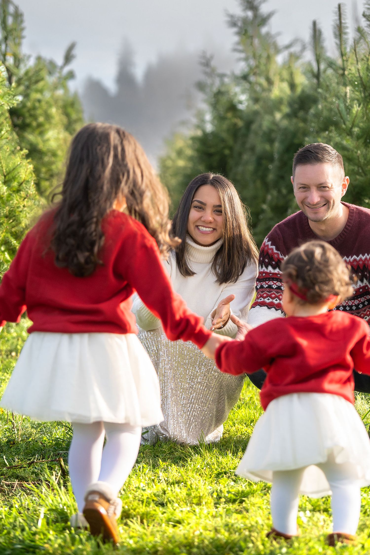 Family enjoying a playful moment together at a Christmas tree farm on a sunny winter day.