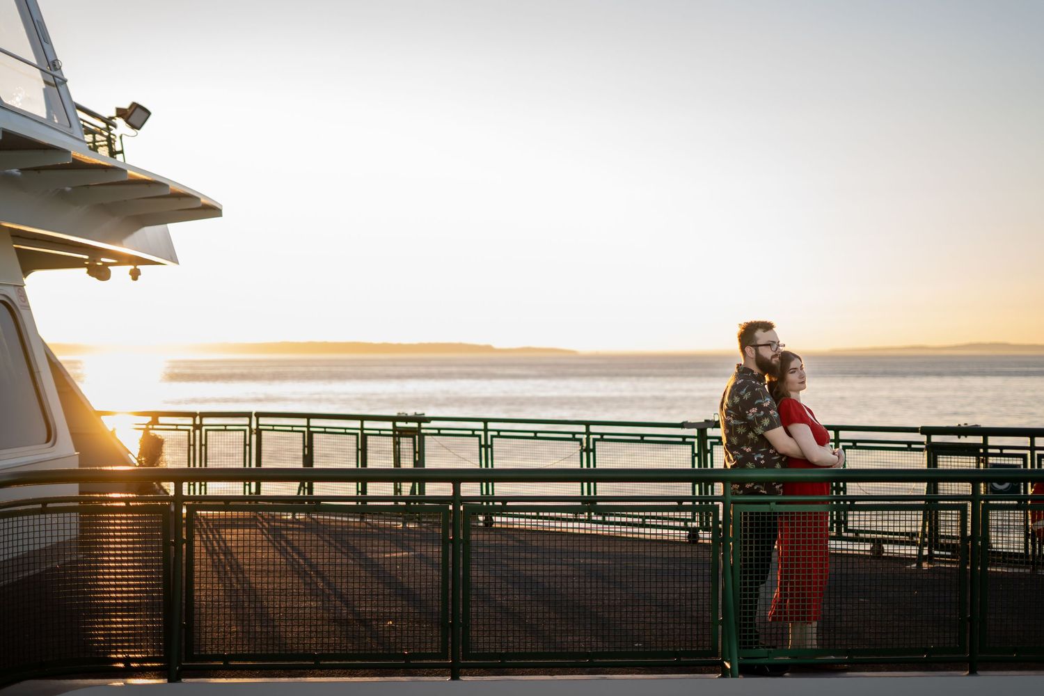 Couple standing on ferry deck during golden hour with water view.