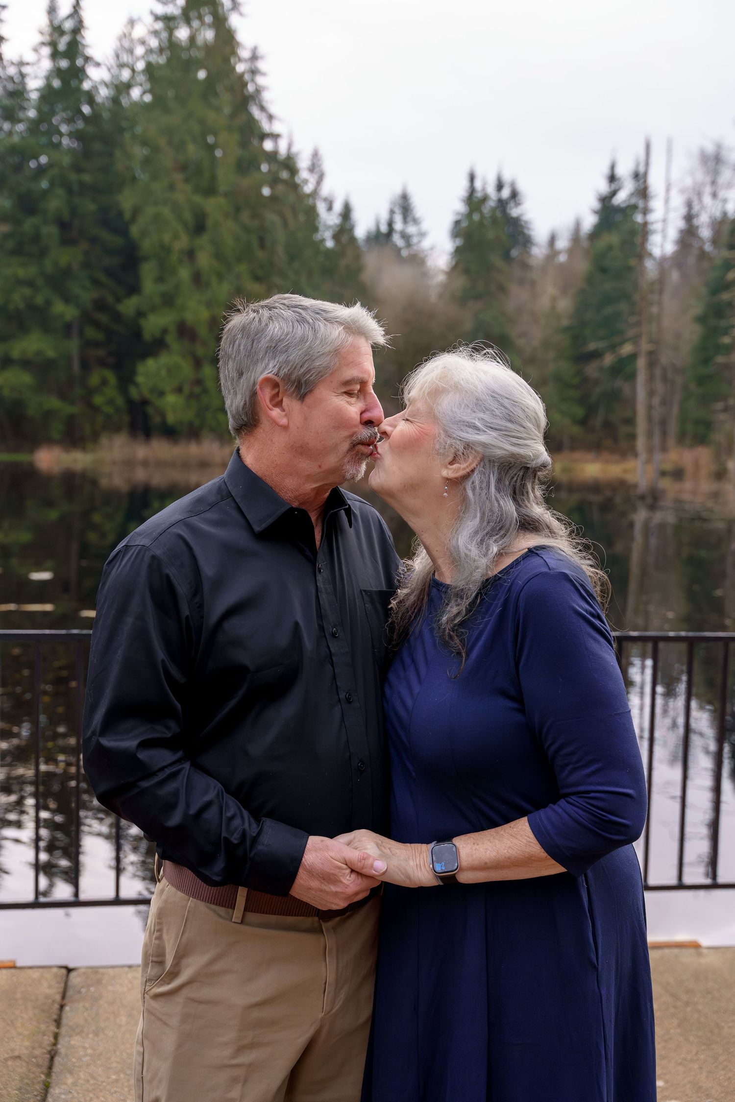 A couple shares a tender kiss outdoors in winter with snow-covered trees in the background.