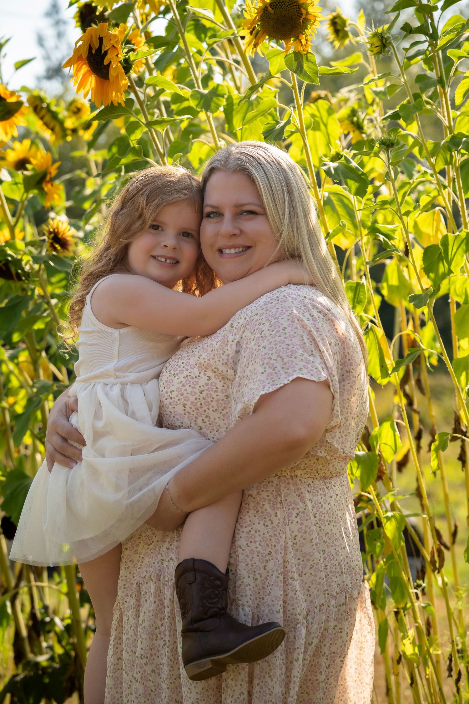 Embracing figures standing in field of tall bright sunflowers during golden hour.