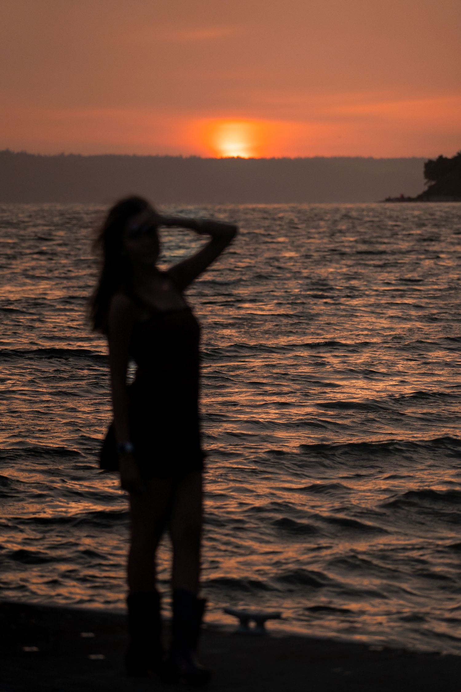 Silhouetted figure dances on beach against dramatic orange sunset over rippling ocean waves.