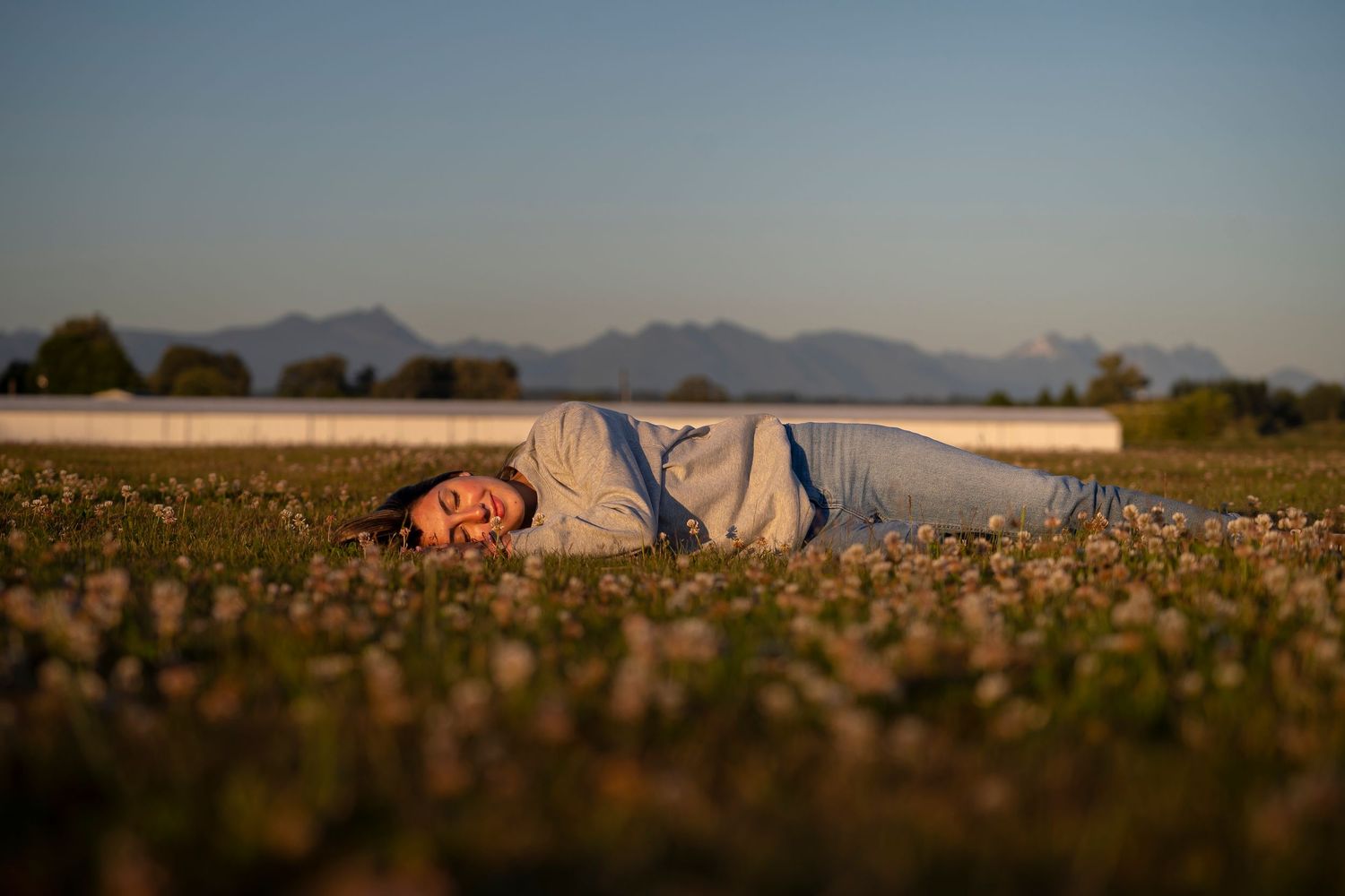 Person lying peacefully in wildflower meadow during golden sunset.