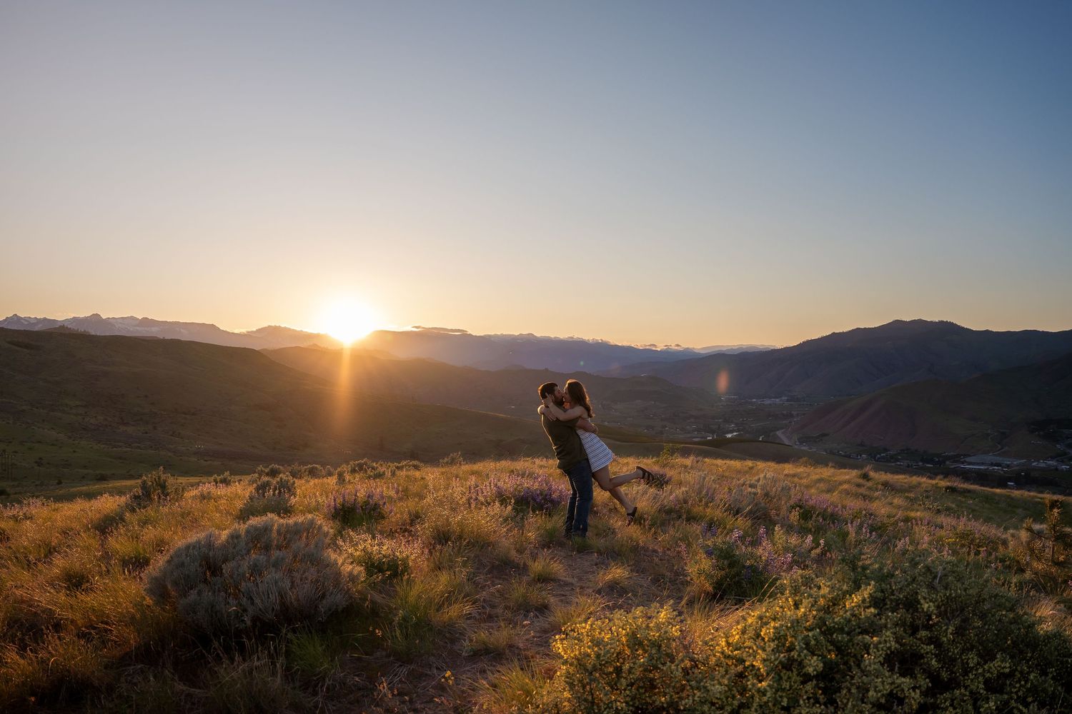 Couple embracing on hilltop during scenic mountain sunset.