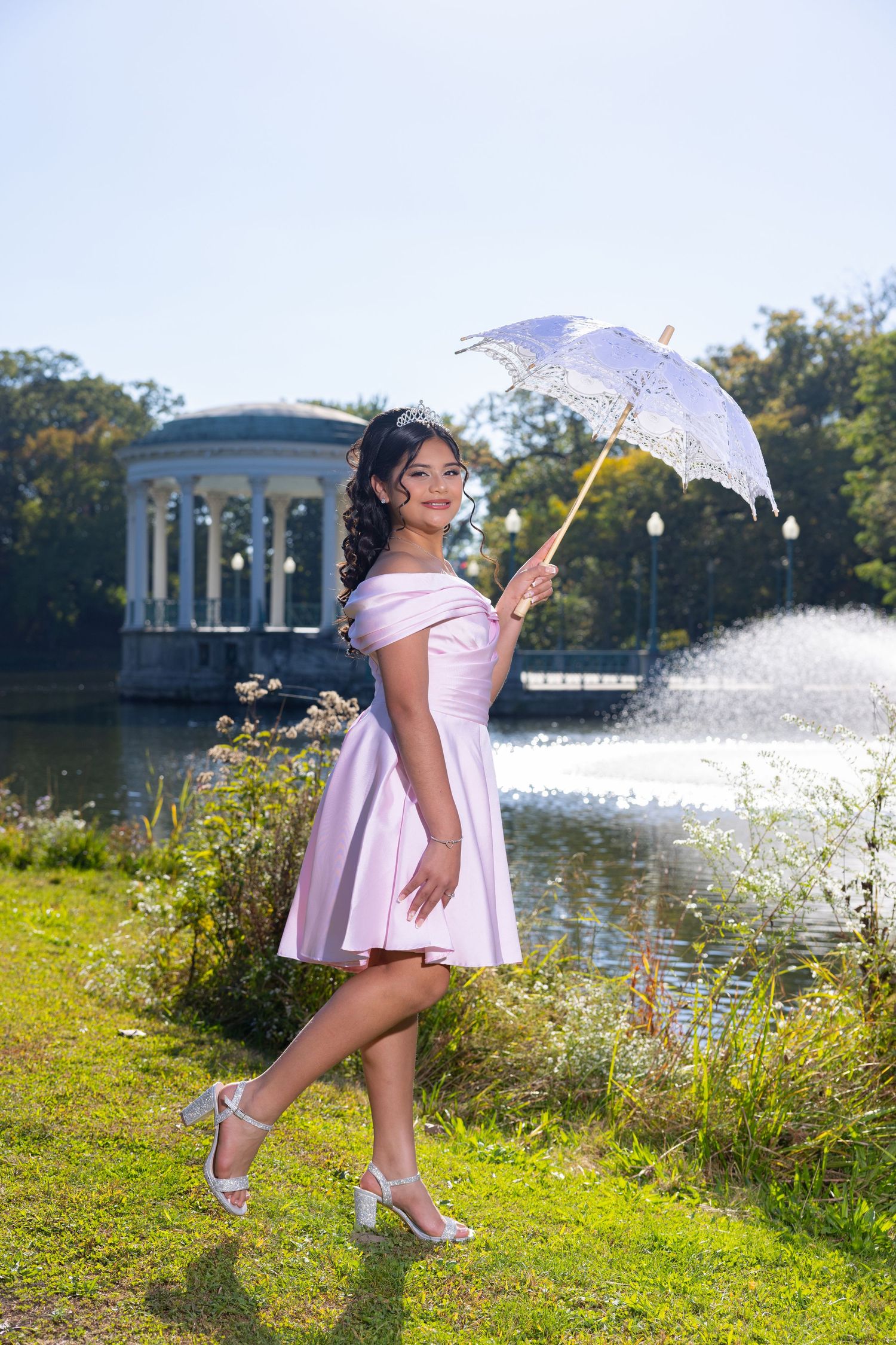Whimsical outdoor photoshoot with lace parasol by lake featuring pink dress and summer scenery.