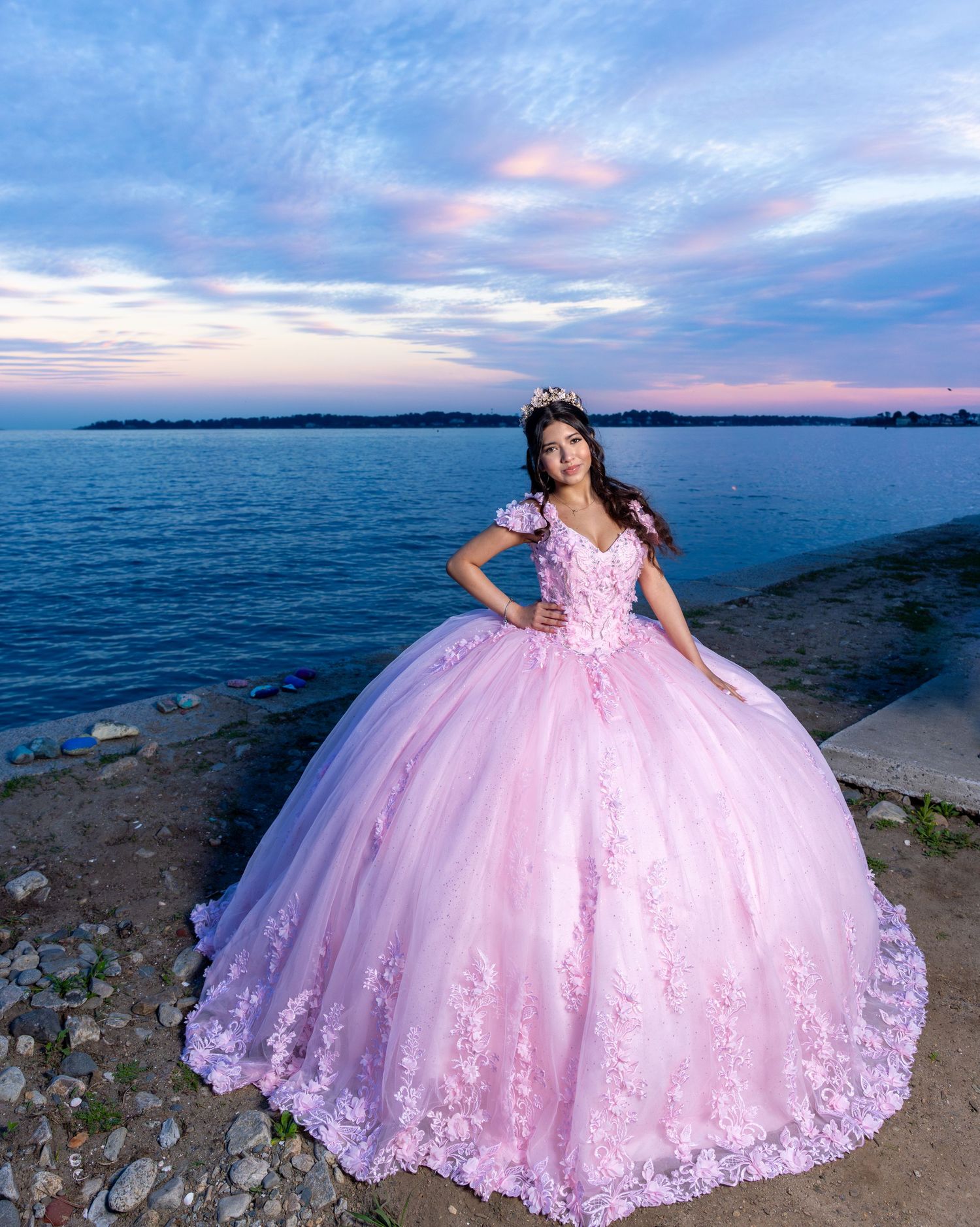 Stunning pink princess ball gown photographed against serene ocean sunset.