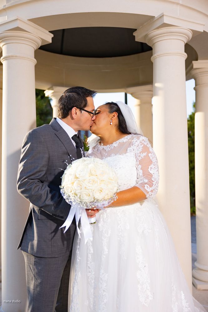 Wedding couple sharing romantic moments under white pillared colonnade.