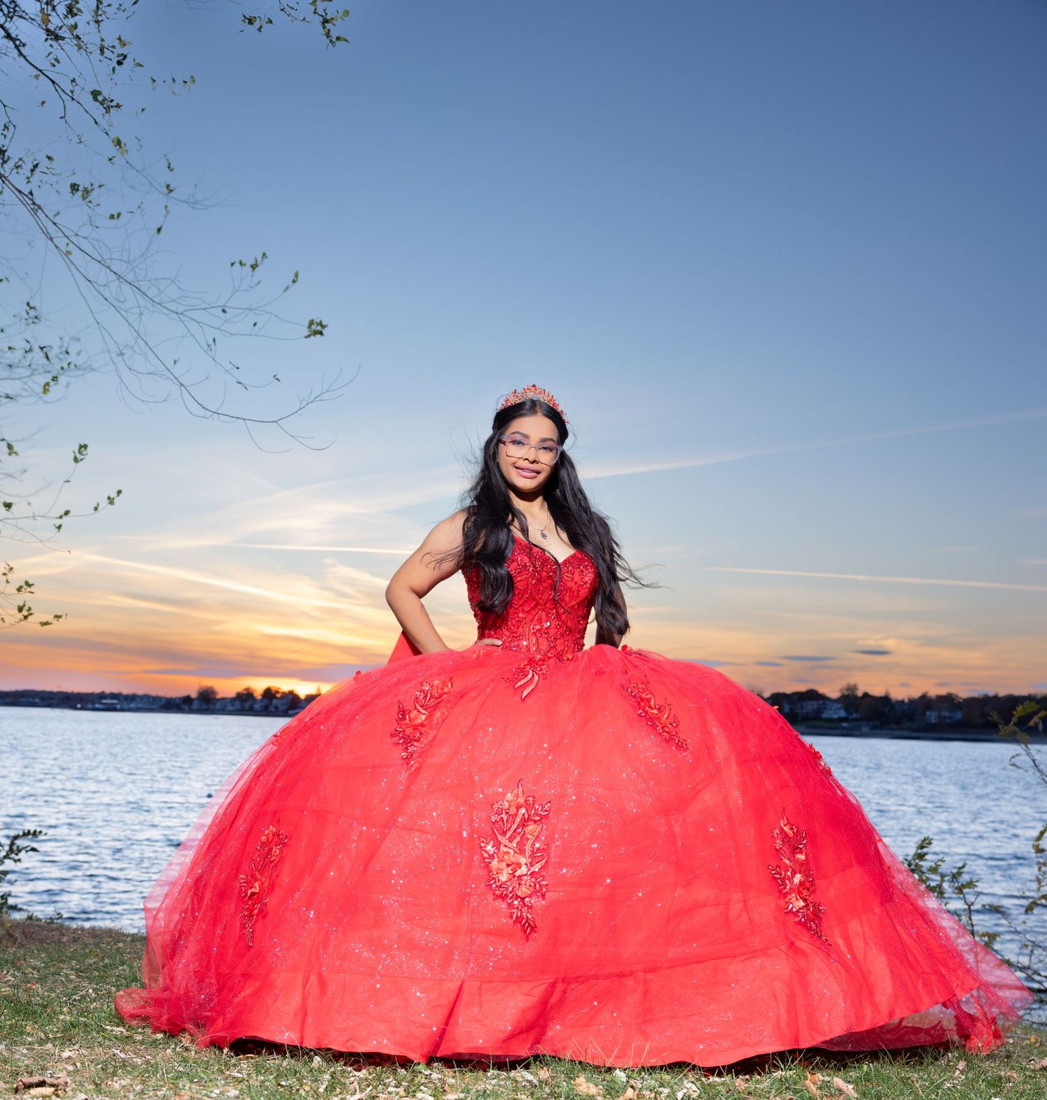 Stunning red ballgown photographed against sunset waterfront backdrop.