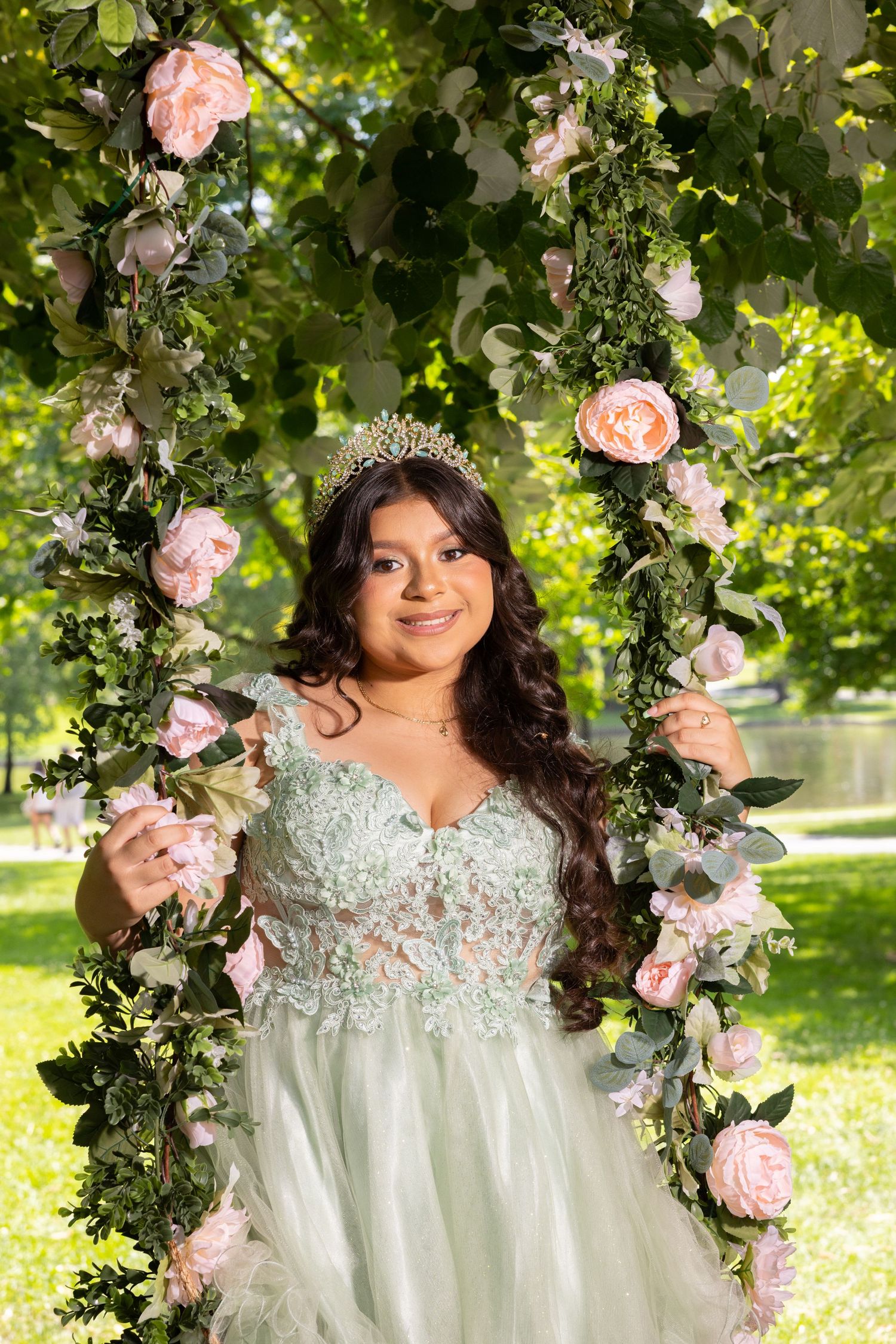 Elegant quinceañera dress with pink roses and greenery arch in outdoor garden setting.