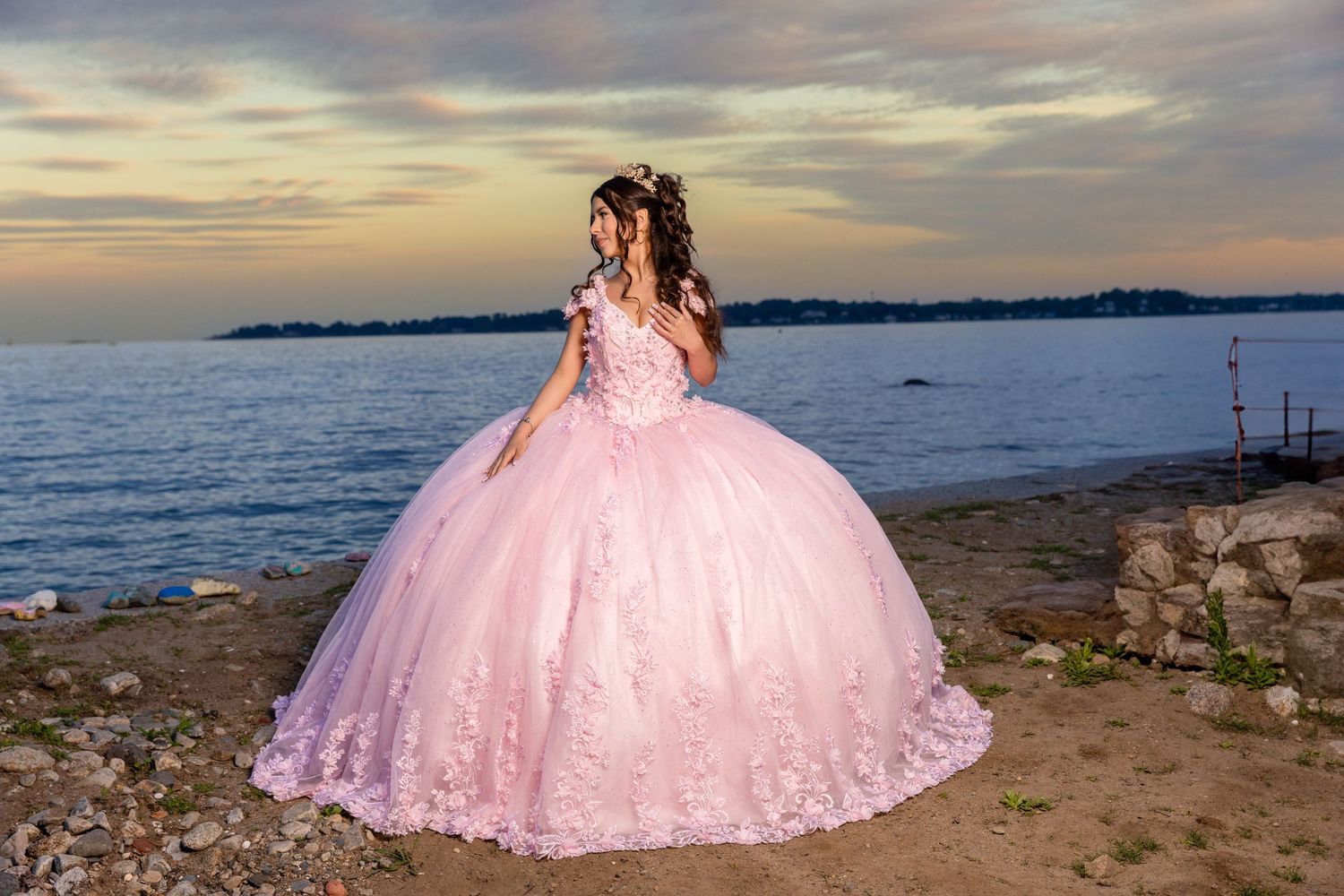 Elegant pink quinceañera dress with lace details captured at rocky beach during golden hour.
