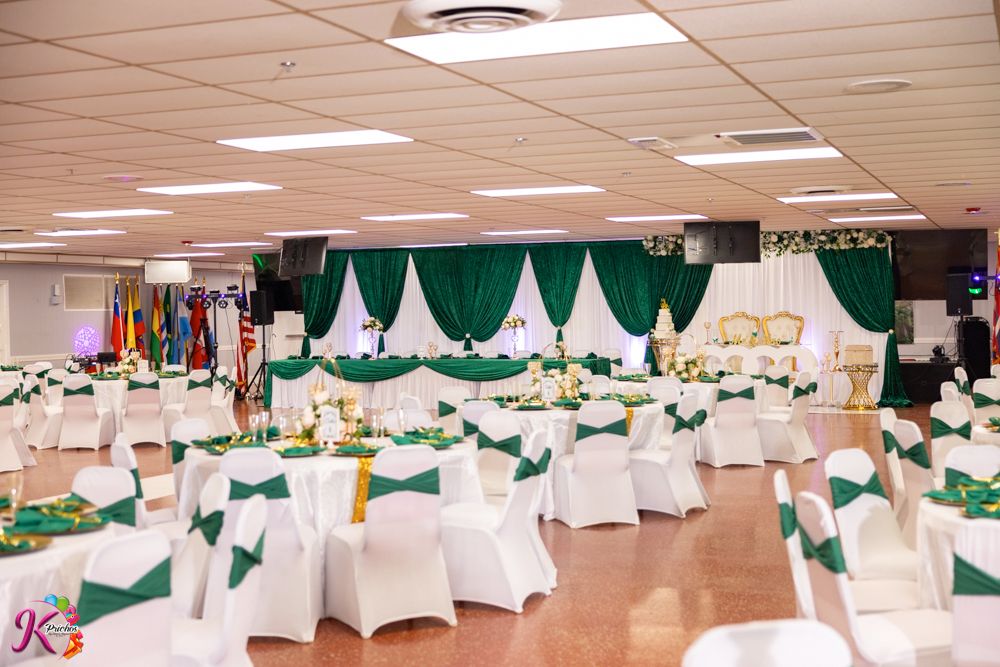 Large banquet hall decorated with white tables, chairs and green drapery for an elegant event setup.