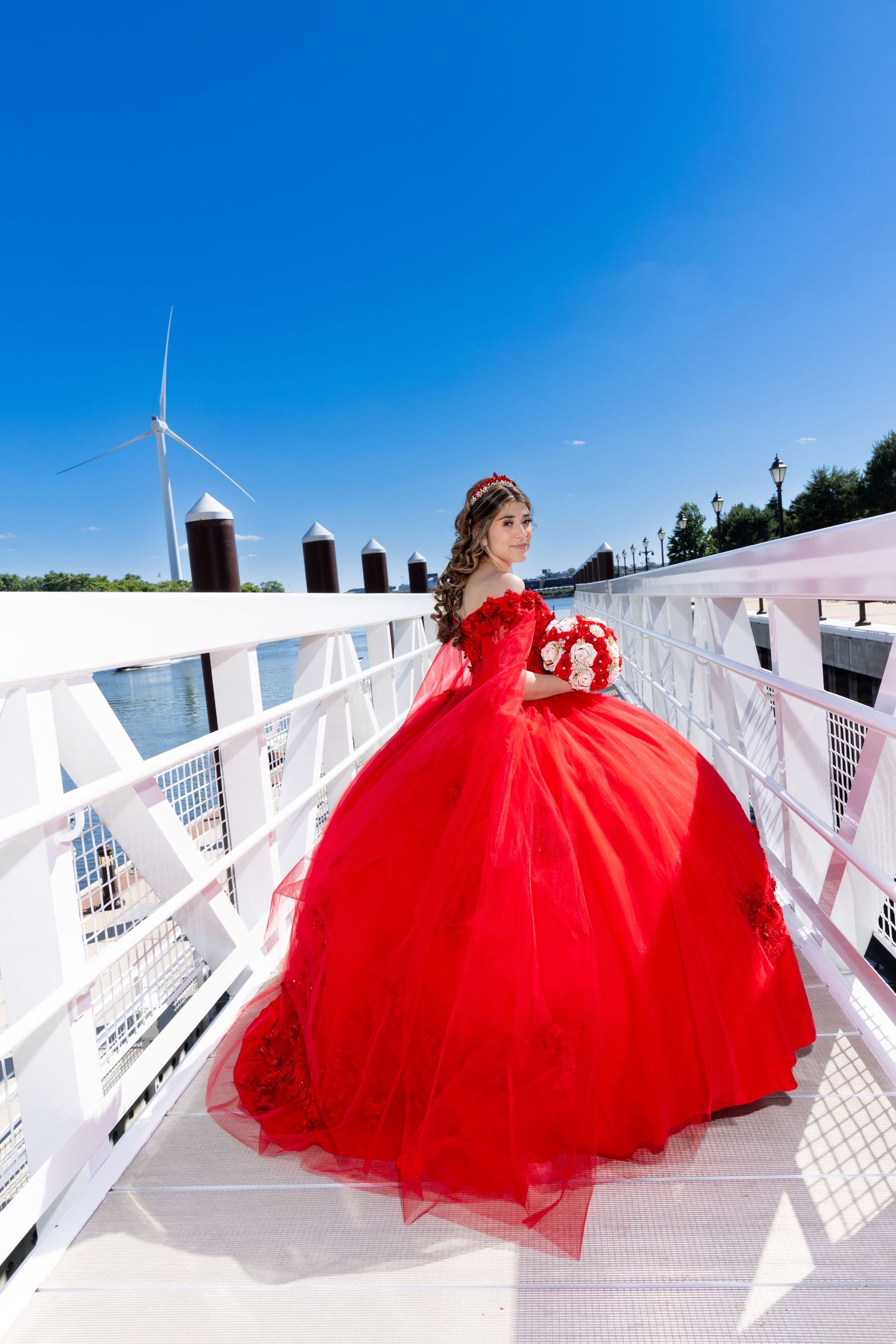 Dramatic red ballgown dress photographed on white boat dock under bright blue sky.