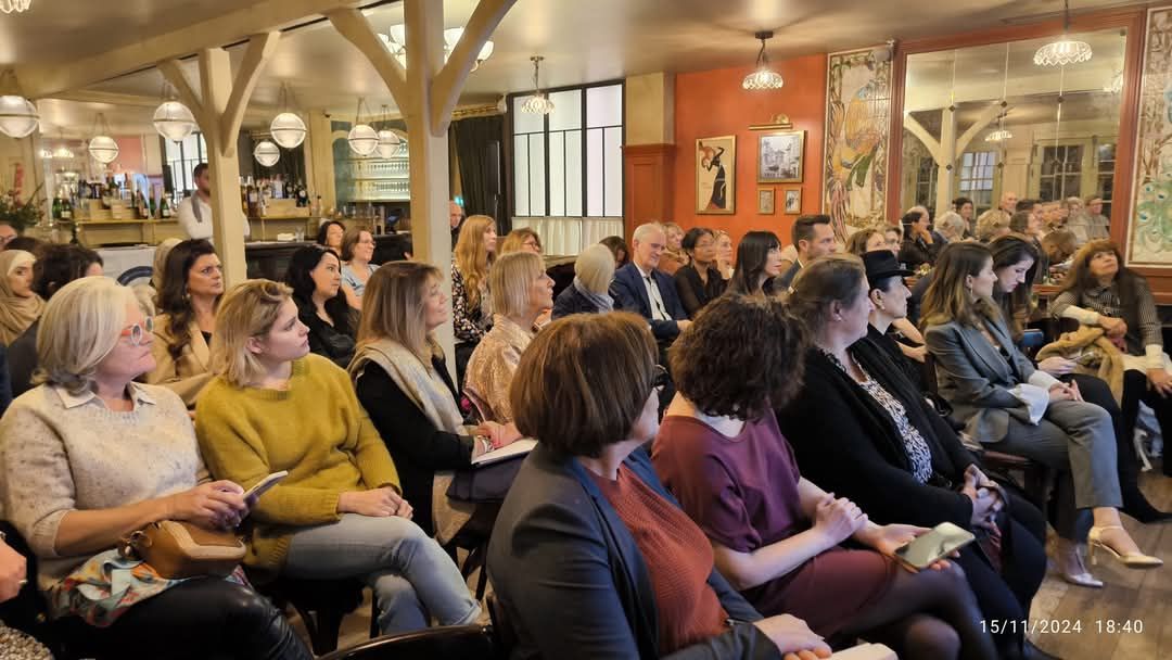 A crowded indoor event with rows of attentive audience members sitting in chairs listening to a presentation.