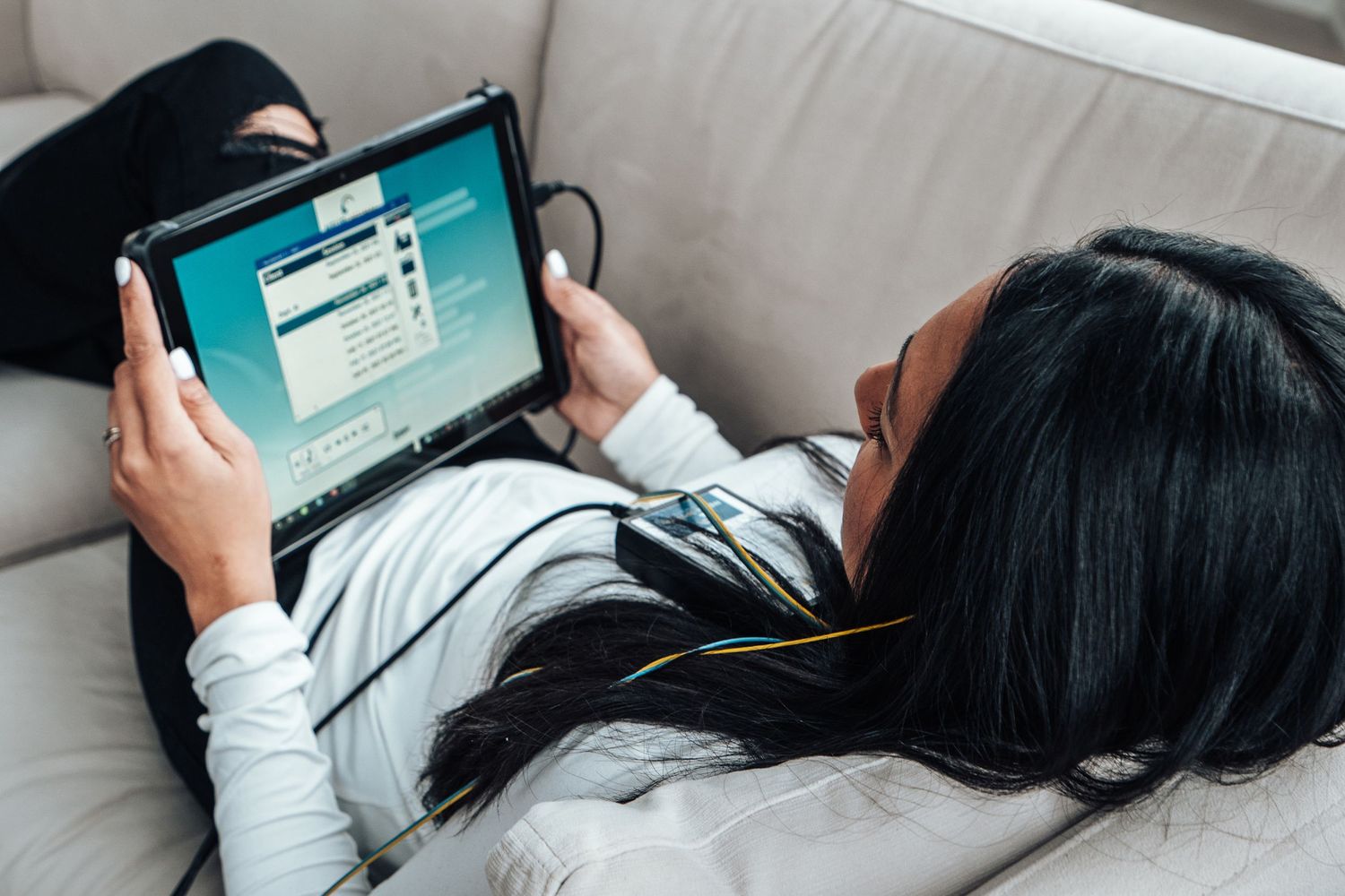 Person lying on bed using tablet device while wearing white long sleeve shirt.