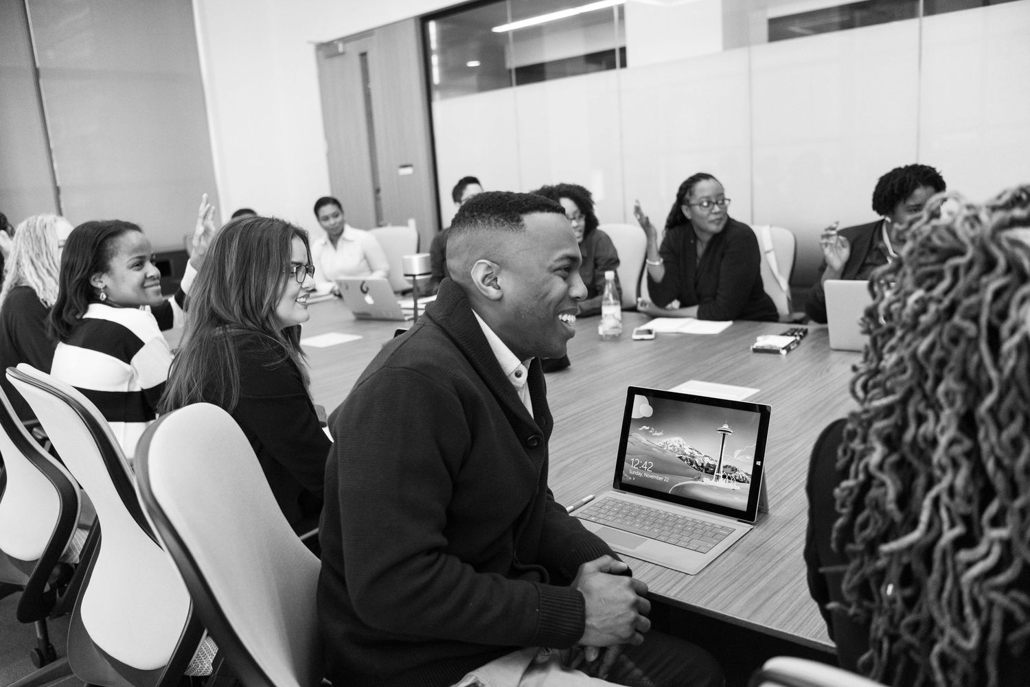A professional meeting shows people seated around a long conference table in an office setting.